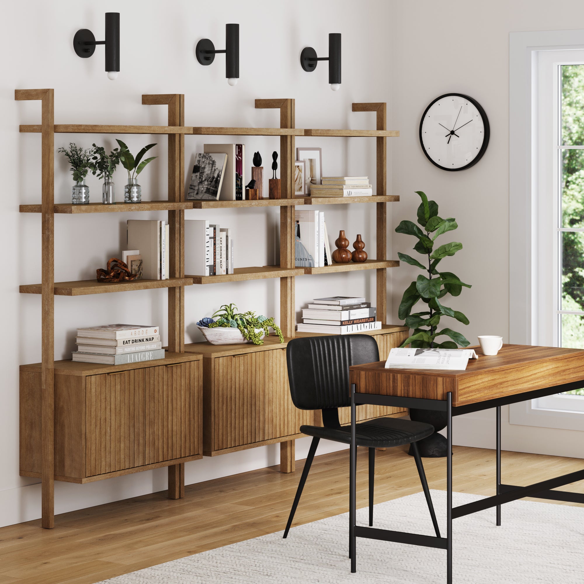 A modern home office features Nathan James Mid-Century Fluted Wall Bookshelves with Doors Light Brown (Set of 3) for books and decor, a wooden desk with black chair, wall clock, tall potted plant, large window, and light wood flooring.