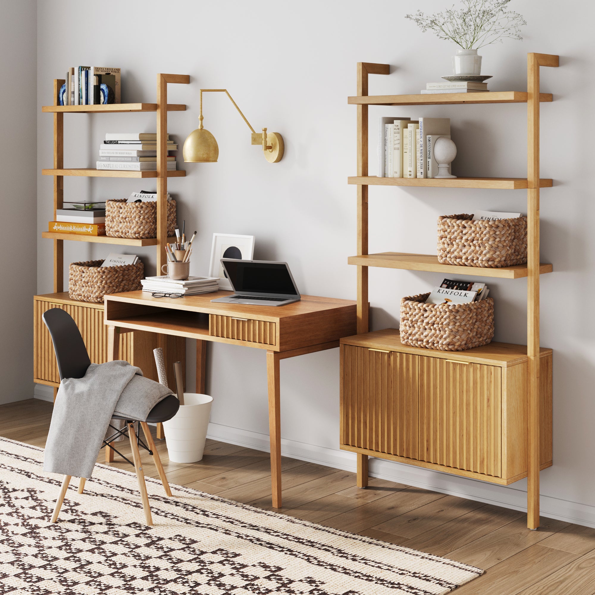A modern home office featuring the Nathan James Mid-Century Fluted Wall Desk, solid wood bookshelves, a laptop, books, woven baskets, decorative accents, a black chair with a throw, and a patterned rug on hardwood floors with neutral decor.