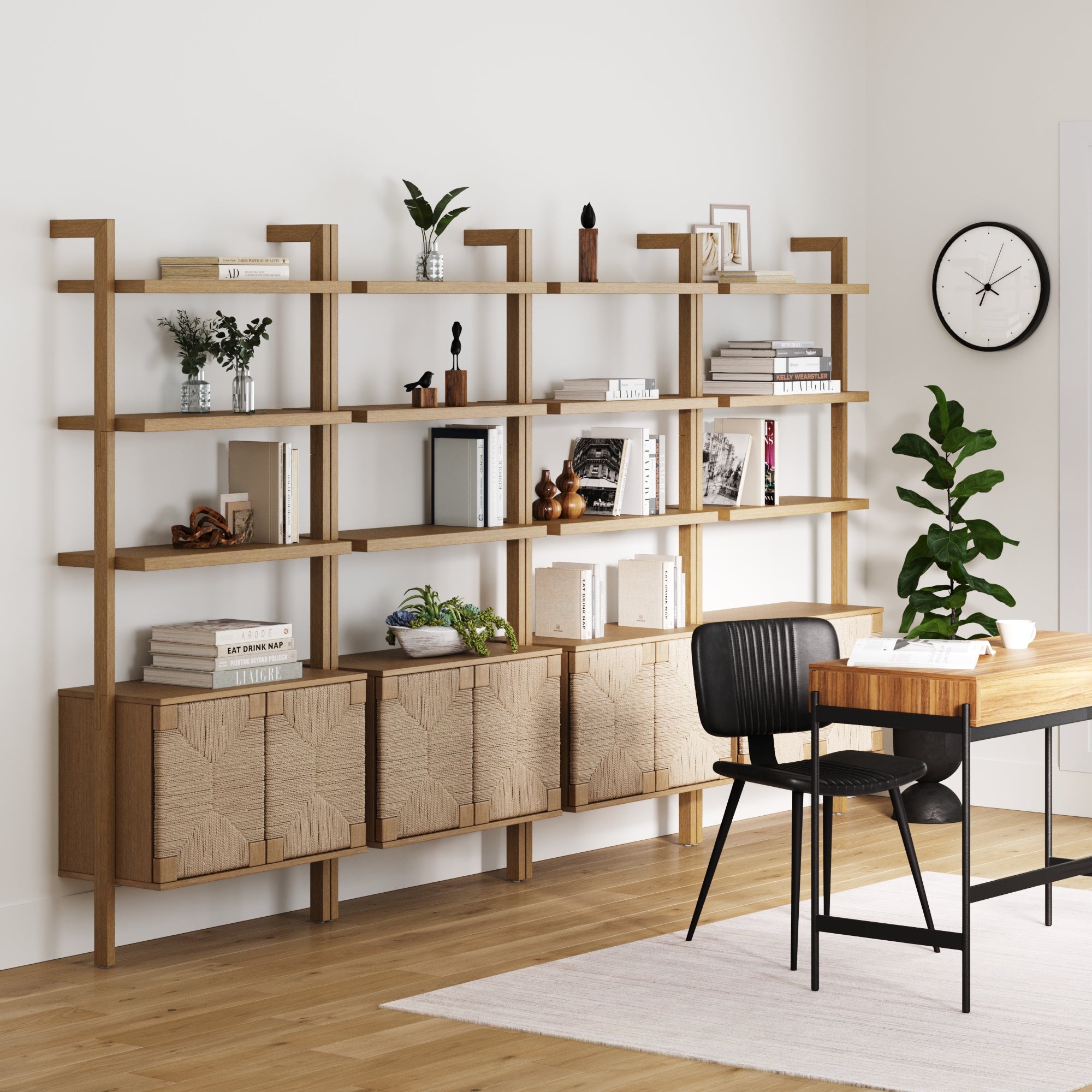 A modern office showcases Nathan James Seagrass Wall Bookshelves with Doors (Set of 4, Light Brown) above cabinets on a white wall. Nearby, a wooden desk and black chair are accented by a wall clock and potted plant.