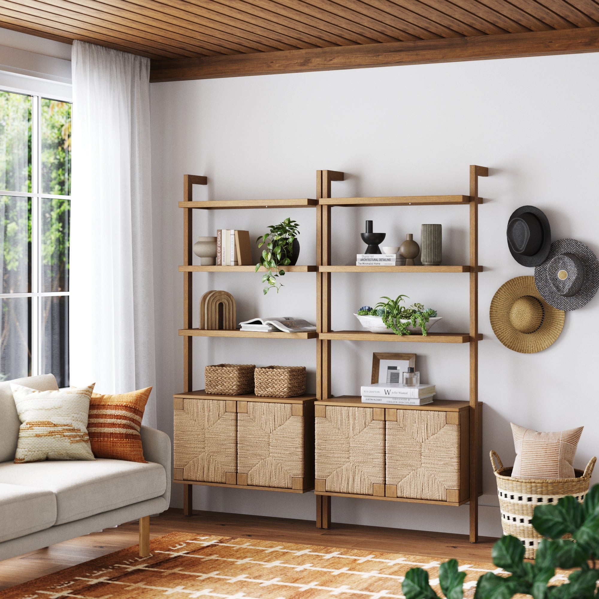 A modern living room with a wooden shelf unit displaying plants, books, and decor. Woven cabinets are below the shelves. A sofa with textured pillows sits nearby. Sun hats and round baskets hang on the white wall.
