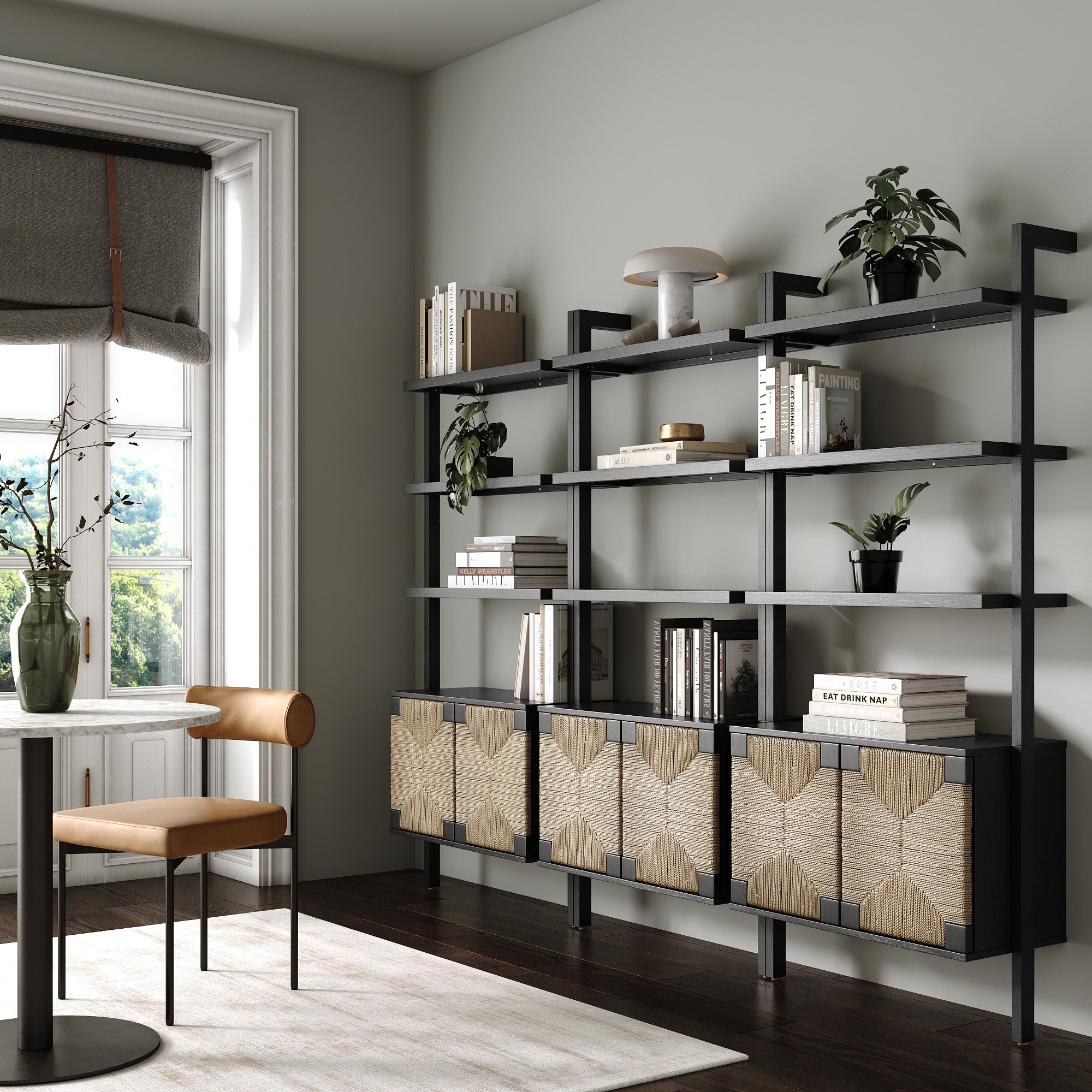 Modern home office with Nathan James Seagrass Wall Bookshelves with Doors Black (Set of 3), hand-woven seagrass fronts, decorative plants, books, a brown chair by a round table, and a window with a grey Roman shade.