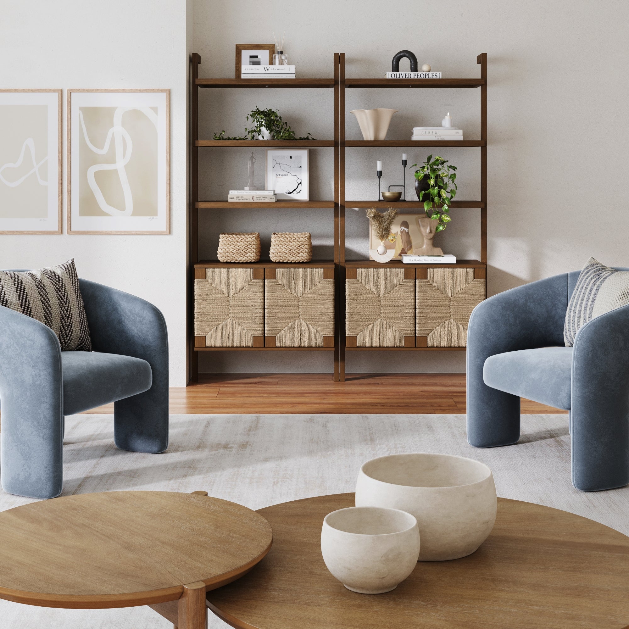 A modern living room with two blue armchairs, a round solid wood coffee table with three decorative bowls, and Nathan James Seagrass Wall Bookshelves with Doors (Set of 2, Dark Brown) displaying plants, books, and décor against a light wall.