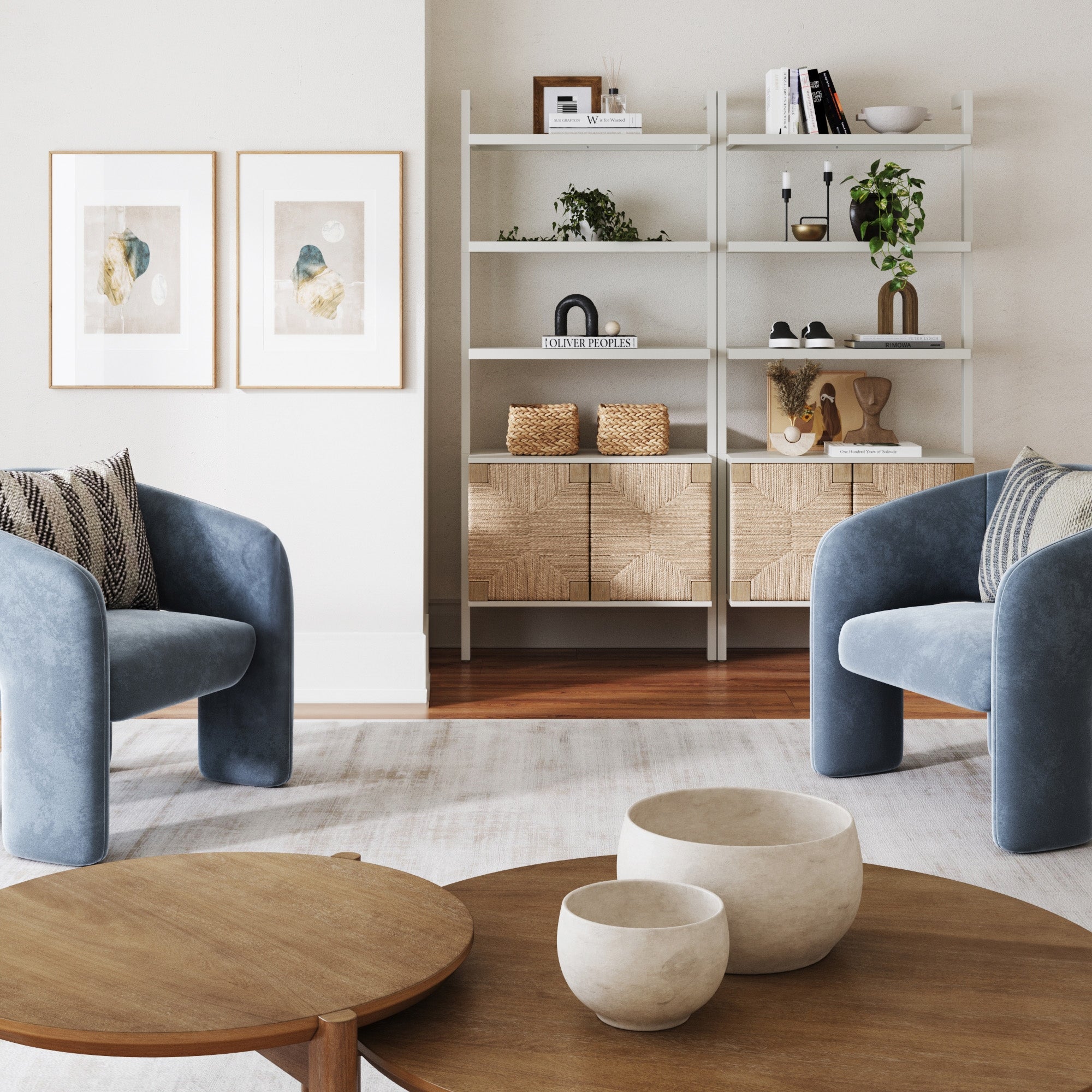 A modern living room with two blue armchairs, a wooden coffee table with decorative bowls, and a Nathan James Seagrass Wall Bookshelf with Doors in white, styled with plants and decor, plus framed abstract art on a light wall.