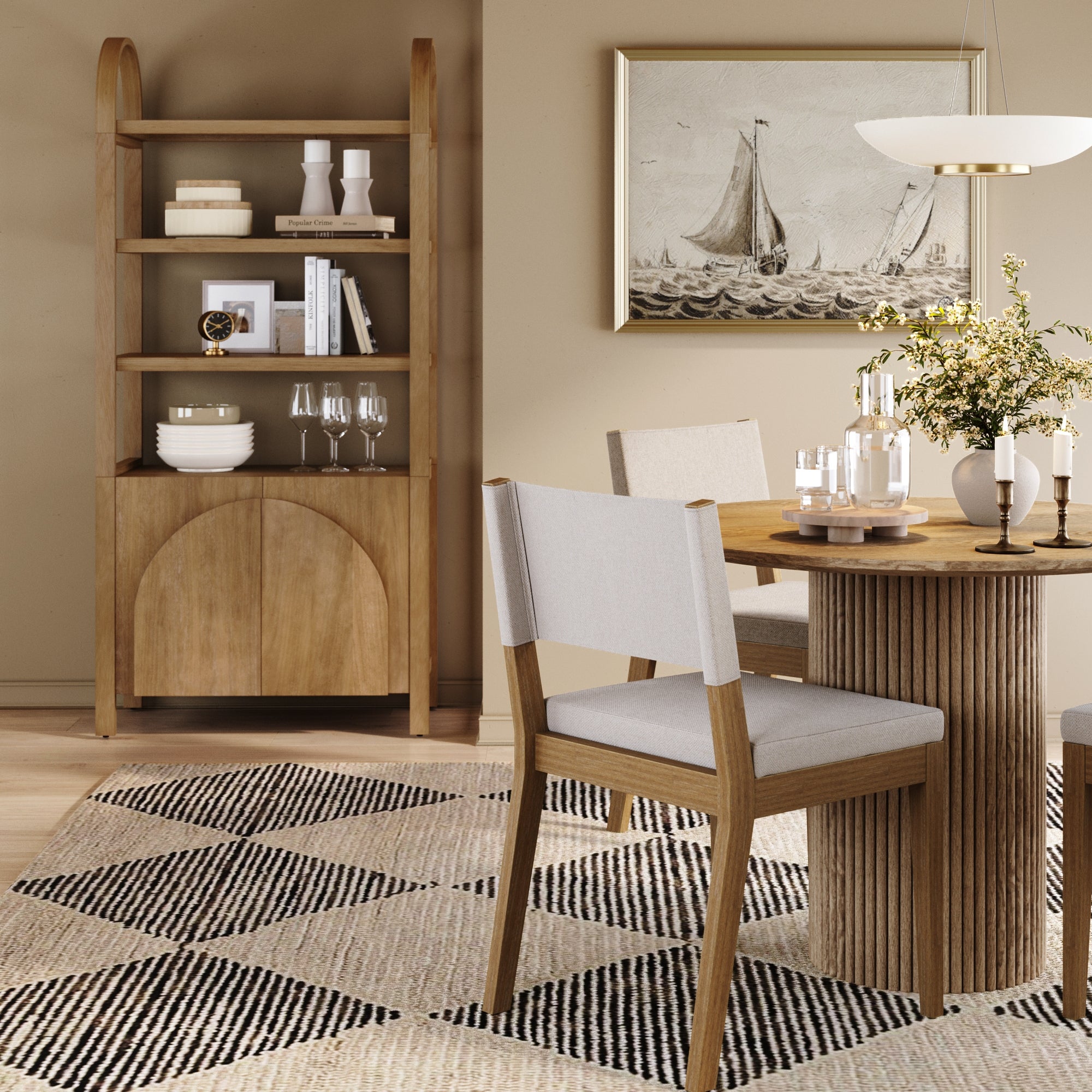 A modern dining room features a round wooden table, beige cushioned chairs, a geometric rug, and the Nathan James Mid-Century Arched Door Bookshelf with Doors in light brown. Framed sailboat art hangs on the beige wall; a vase of flowers sits on the table.