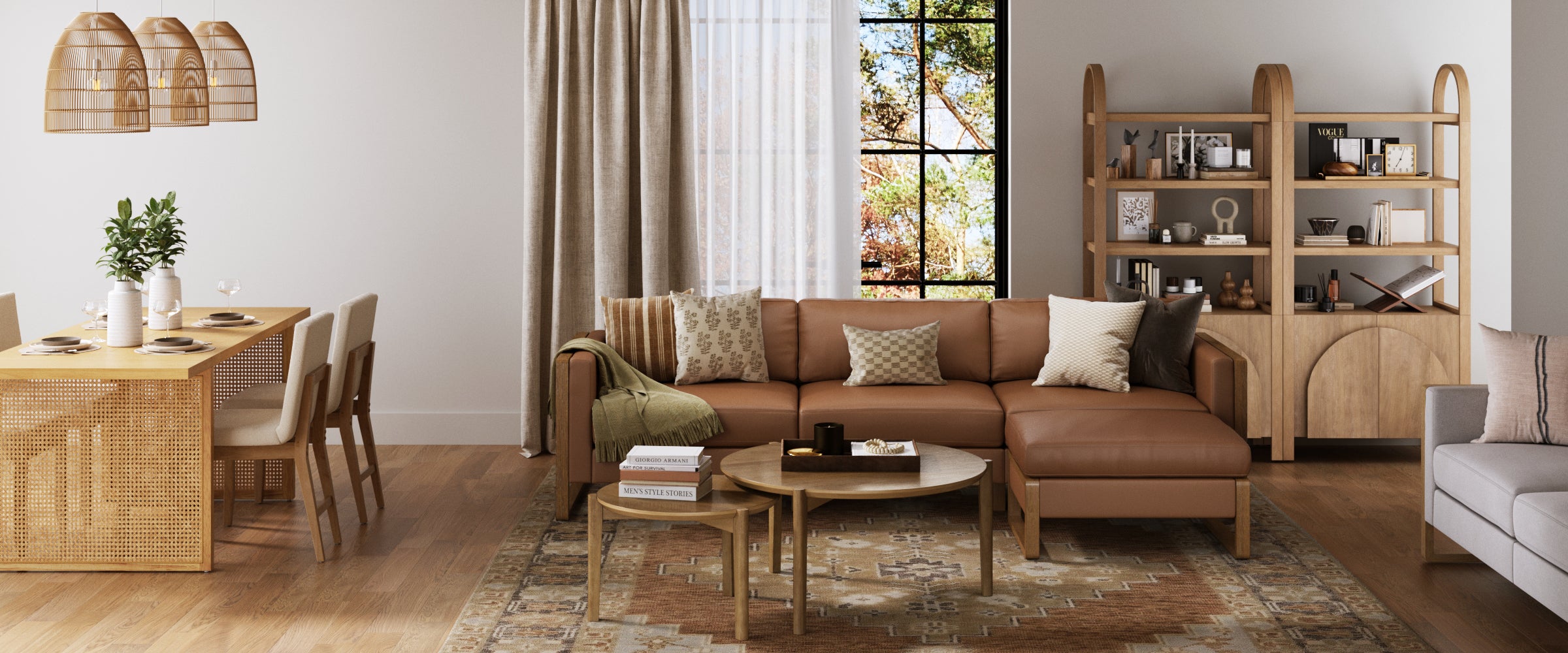 A modern living and dining area with a brown leather sectional sofa, patterned rug, wooden coffee tables, stylish shelves, and a dining table with chairs. Large window with curtains lets in natural light; neutral and wood tones dominate the decor.