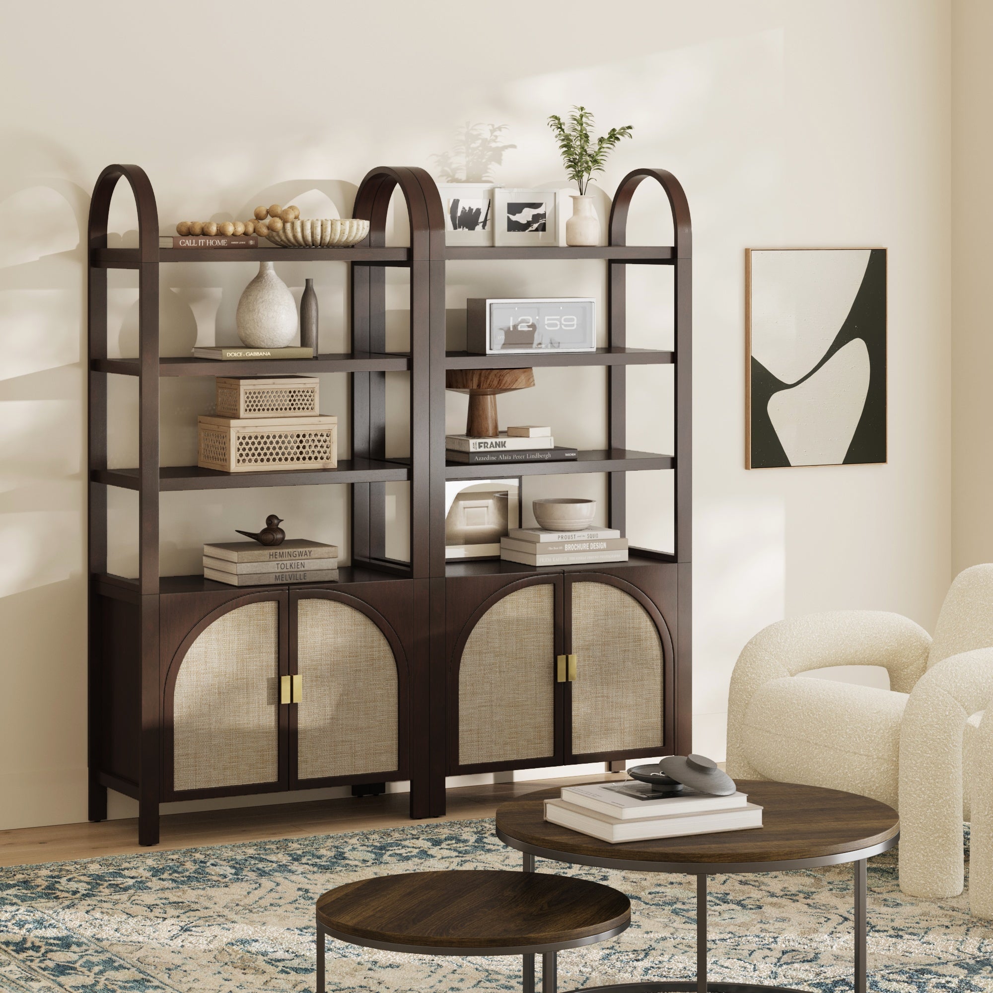 Two dark wood bookshelves with arched tops hold decor, books, and baskets. Cabinets with woven fronts are below. A round coffee table, armchair, blue patterned rug, and abstract wall art complete the modern living room.