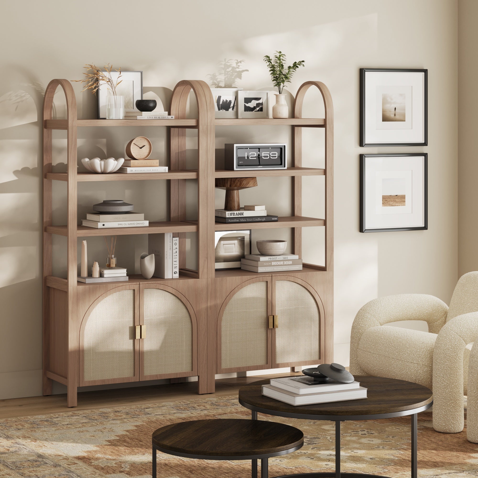 The Nathan James Arched Door Rattan Bookshelf with Doors in Raw Oak (Set of 2) holds books, decor, and a clock. Framed art hangs on a beige wall, while a round coffee table and cream armchair complete the sunlit living room.