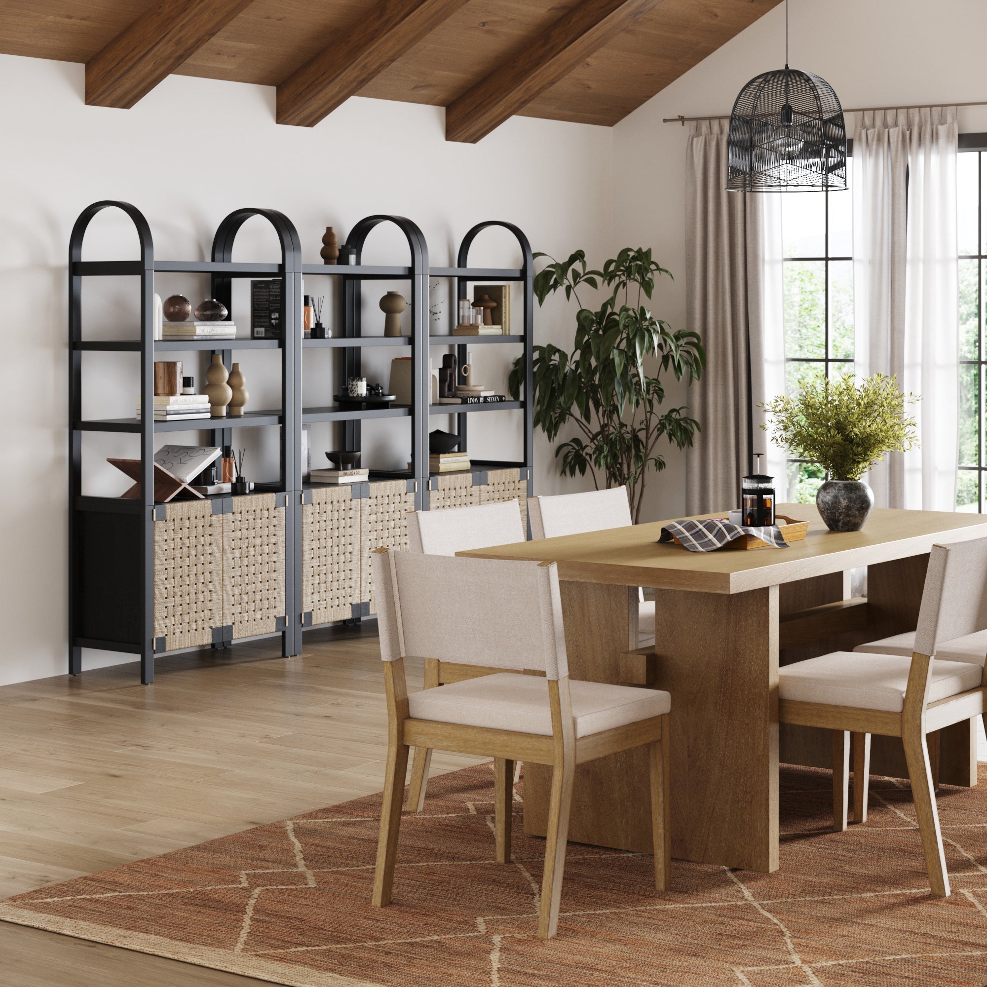 Modern dining room with a wooden table, six beige chairs, a geometric rug, potted plant, sunlit window with curtains, and a set of three Nathan James Boho Woven Seagrass Bookshelves in black for stylish boho elegance.