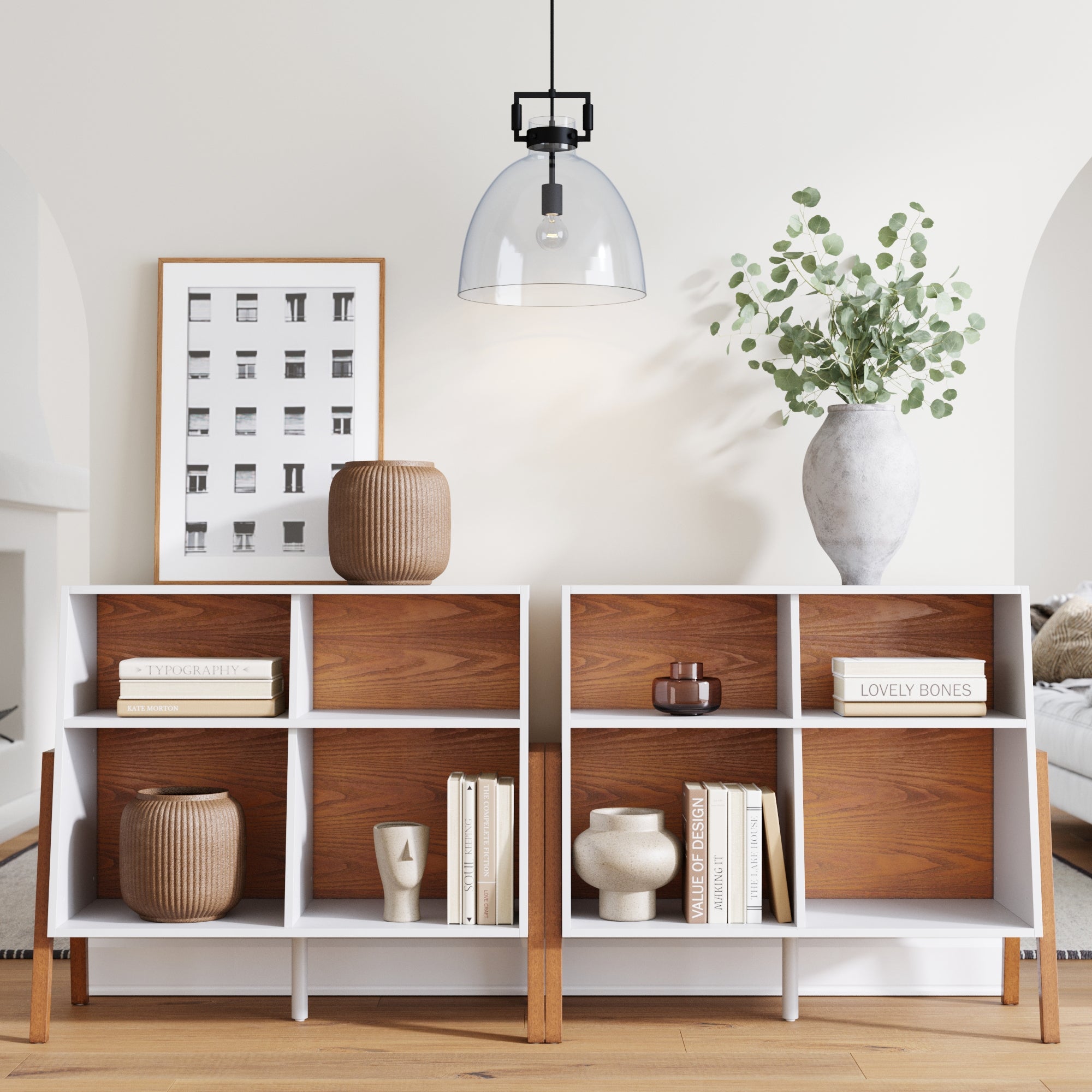 Two Nathan James Mid-Century TV Consoles (Set of 2) display books, vases, and Scandinavian decor. A large vase with green branches sits atop one. Above the minimalist living space are a framed black-and-white photo and a pendant light.