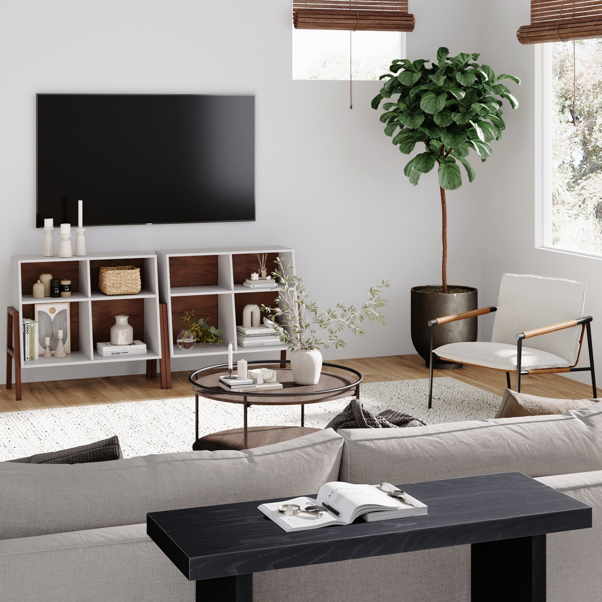 A modern living room with a gray sofa, black console table, round glass coffee table, white armchair, large TV on the wall, shelves with decor, a potted plant, and sunlight streaming through windows with wooden blinds.