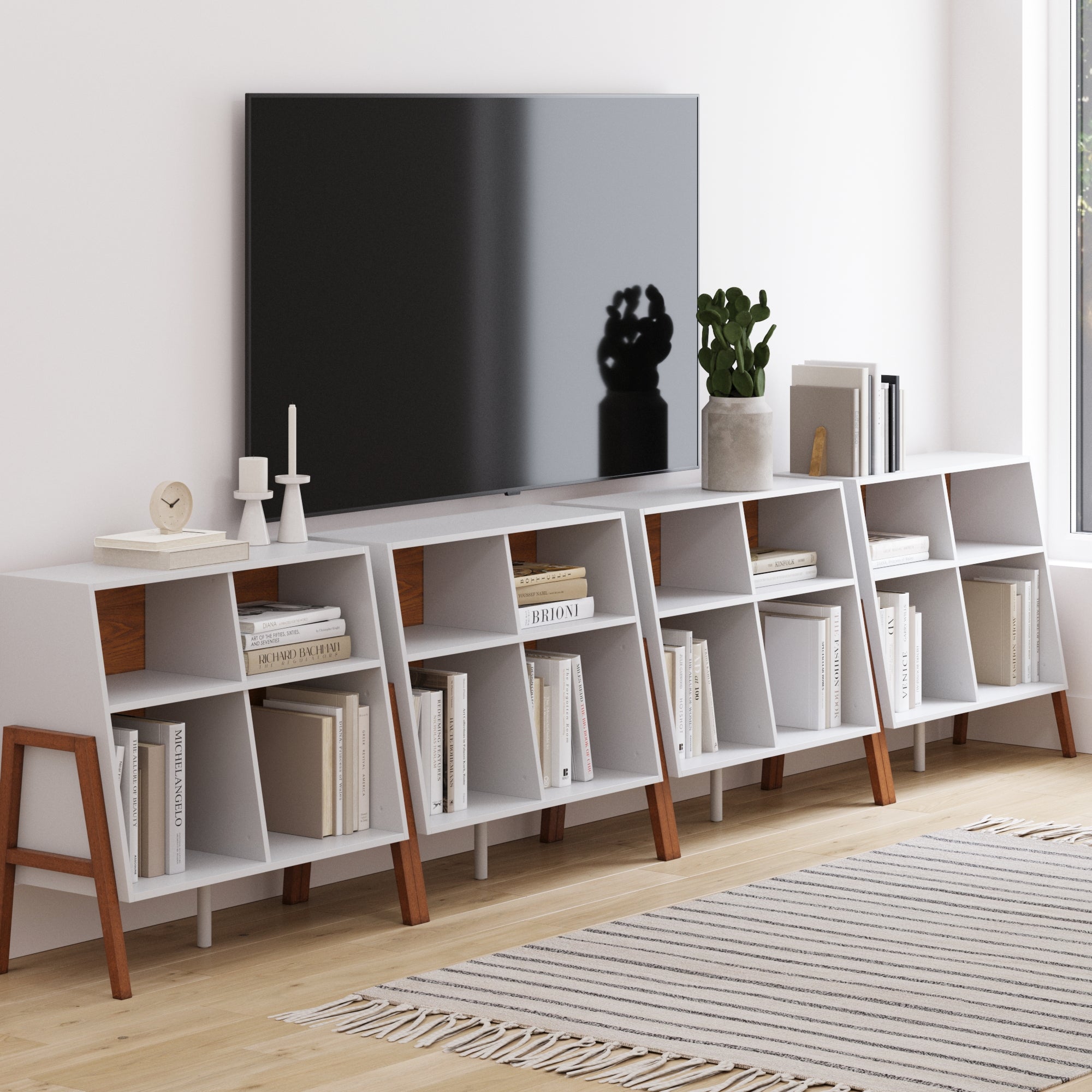 A modern Scandinavian living room features a large flat-screen TV above the Nathan James Large Mid-Century Open Storage Unit (Set of 4), styled with books, decor, a plant, and candles on a light wood floor with a striped rug.