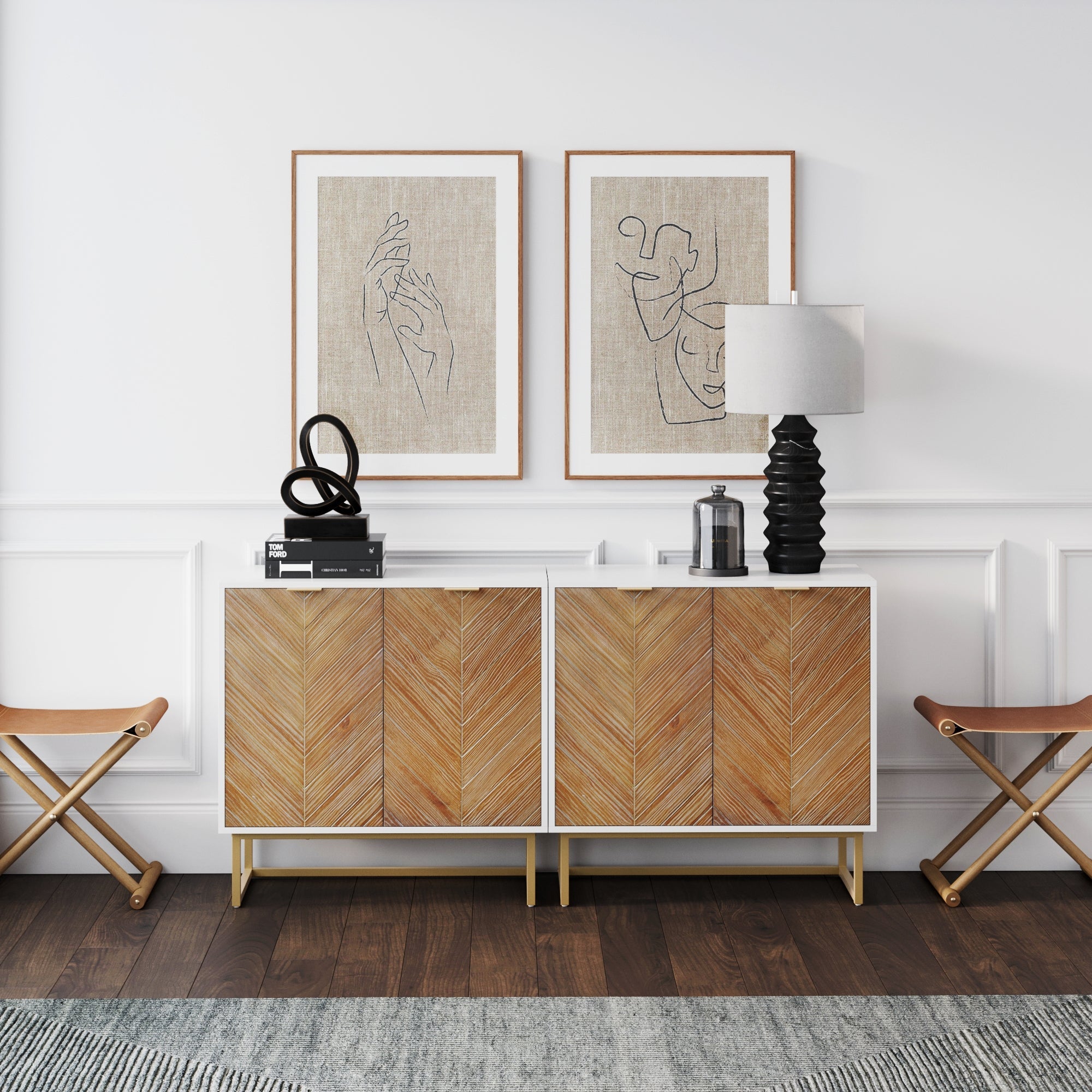 A modern living room features two Nathan James Wood Herringbone TV Console Credenzas in white, paired with abstract line art prints above, a sculptural black decor piece, a lamp, and folding stools against a white paneled wall.