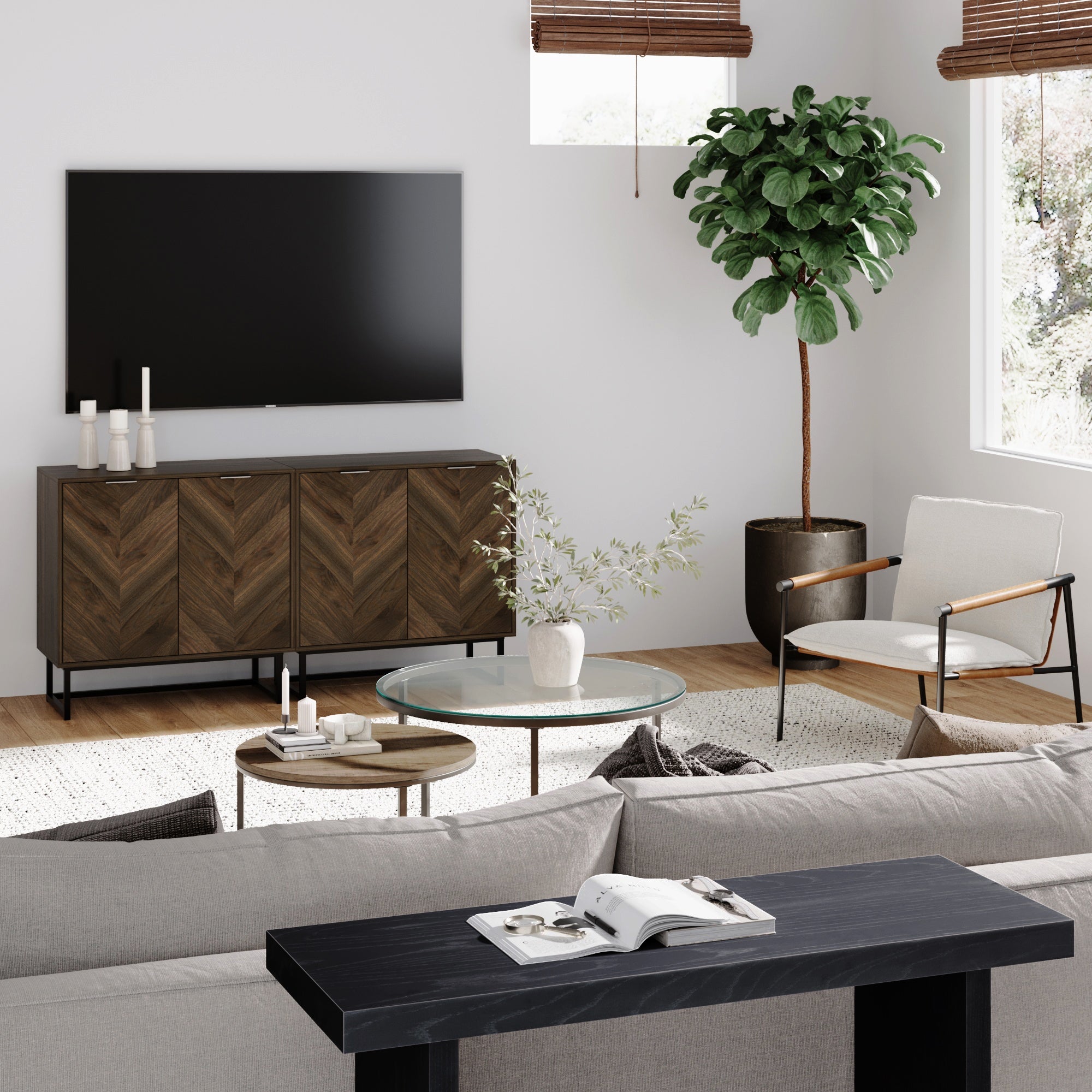 Modern living room with a sofa, a glass coffee table, an armchair, a wooden sideboard with candles, a large flat-screen TV on the wall, a tall potted plant, and sunlight streaming through window blinds.