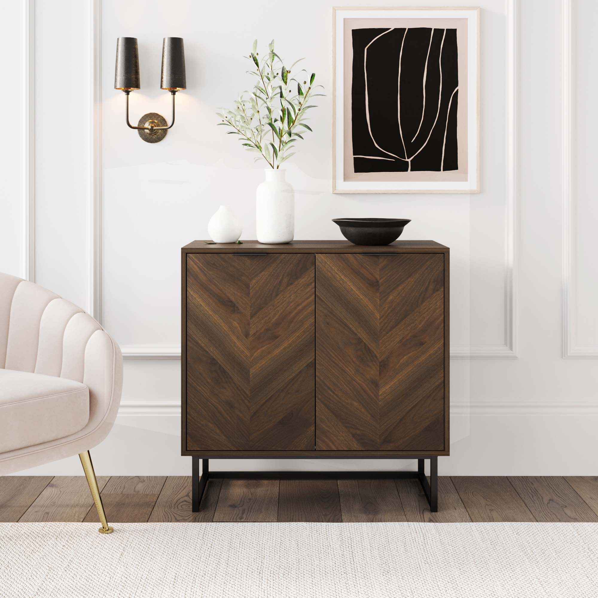 A modern room showcases the Nathan James Wood 2-Door Storage Cabinet Walnut with a bold herringbone pattern, styled with white vases and a black bowl. Above, abstract art and a black sconce add flair. A beige chair is positioned to the left.