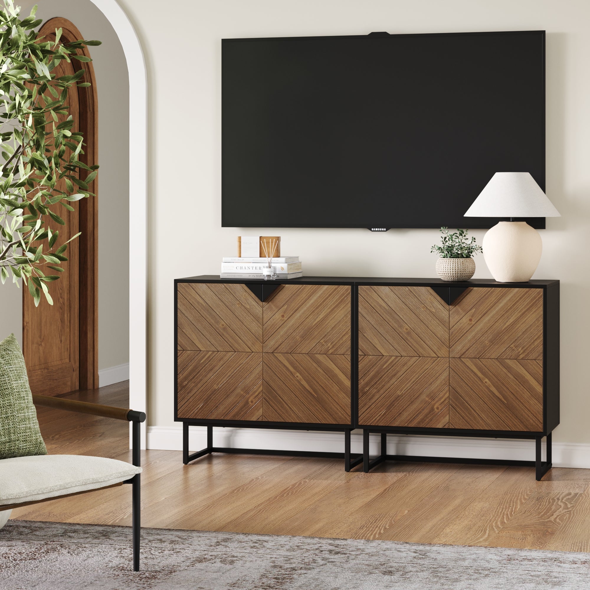 A modern living room features the Nathan James Brushed Fir TV Console Credenza (Set of 2) with a mounted flat-screen TV, decorative books, a lamp, a potted plant, and a chair with a green cushion for cozy seating.