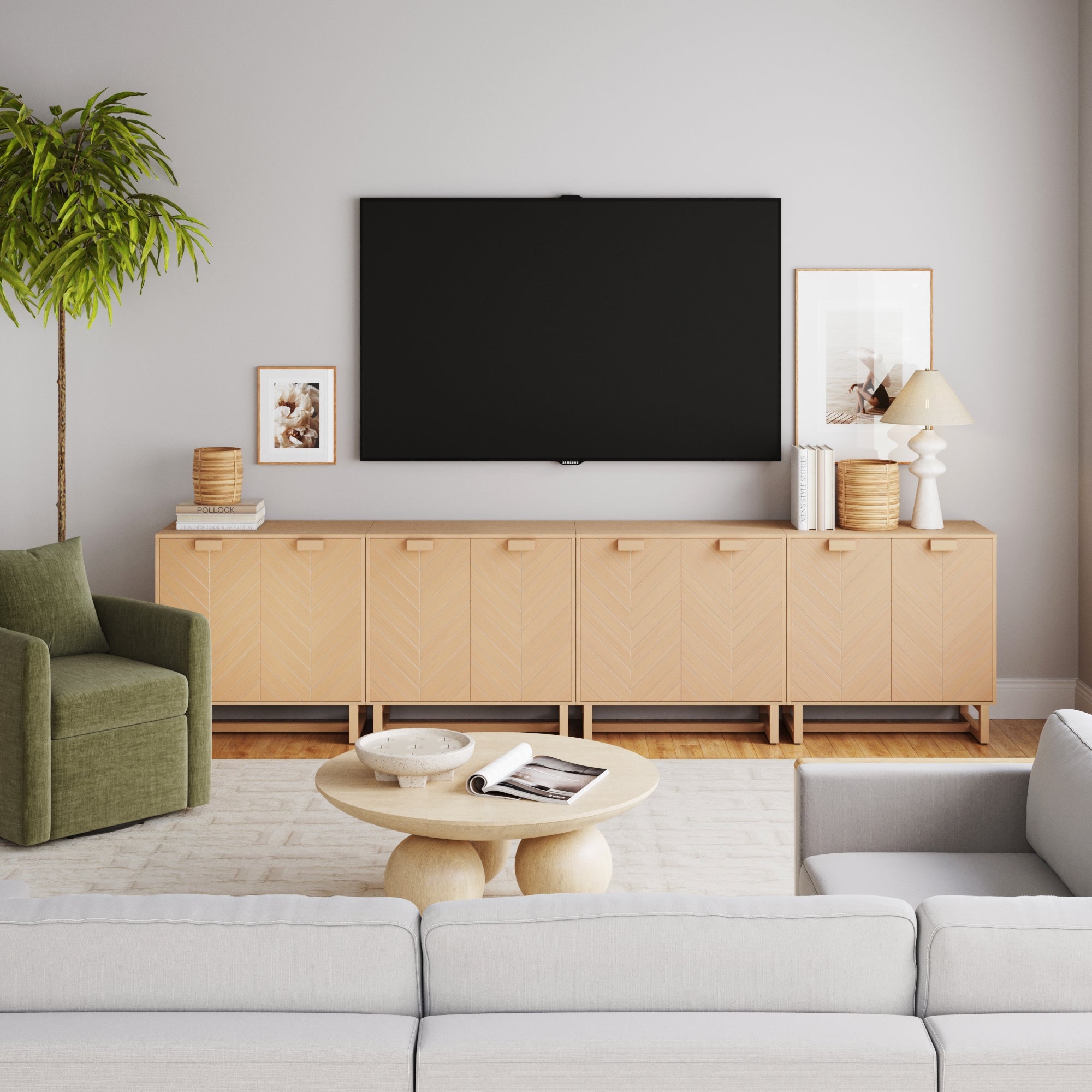 A modern living room features a large black TV above the Nathan James Wood Herringbone 2-Door Credenza in Raw Oak (Set of 4), neutral decor, a potted plant, framed art, an olive green armchair, round coffee table, and light gray sofa.