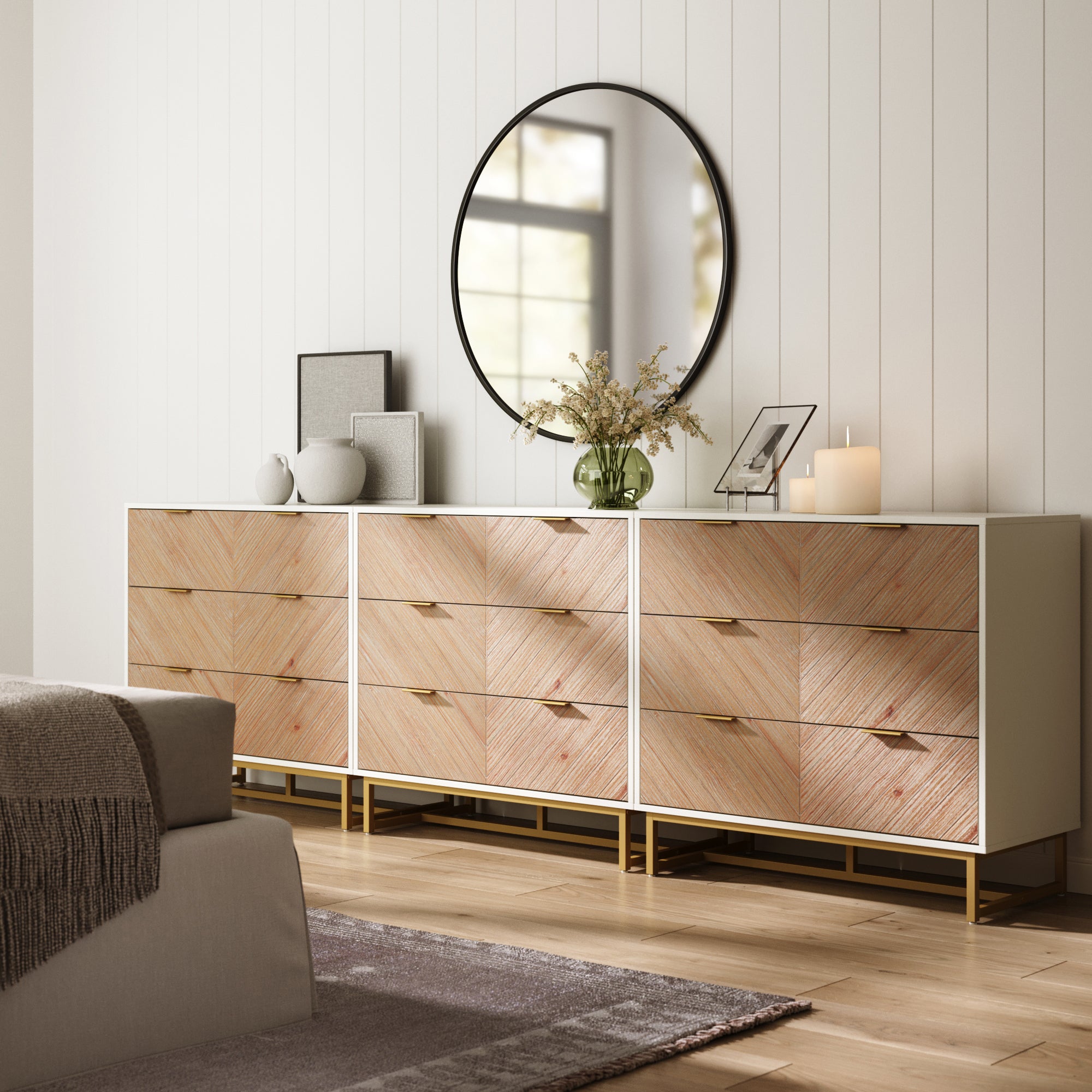 A modern bedroom highlights the Nathan James Boho Herringbone 3-Drawer Dresser in white (set of 3) with gold accents, topped with a round mirror, vases, framed art, candles, and a green plant; a bed with cozy textiles appears in front.