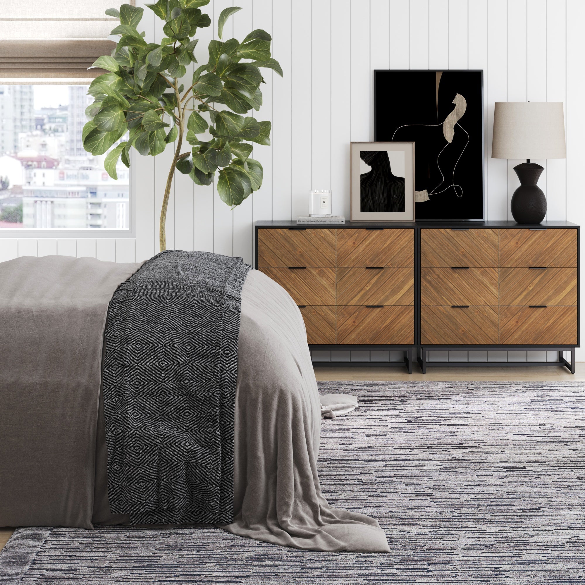 A modern bedroom features a bed with neutral linens and a black geometric blanket, a large potted plant, two Nathan James 3-Drawer Brushed Fir Dressers with art, a lamp and decor, plus a window revealing a city view.