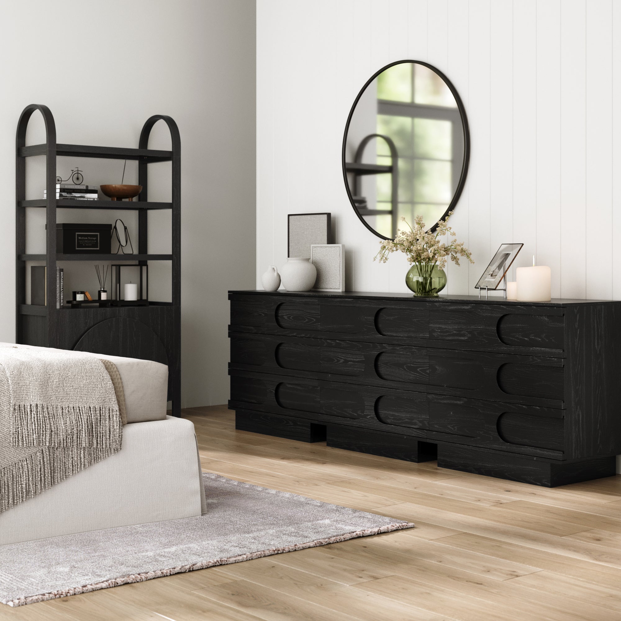 Modern bedroom featuring the Nathan James Mid-Century 3-Drawer Arched Dresser Black Oak (Set of 3), styled with décor, a large round mirror above, a shelf unit, beige bed with textured blanket, and neutral rug on light wood floor for a chic vibe.