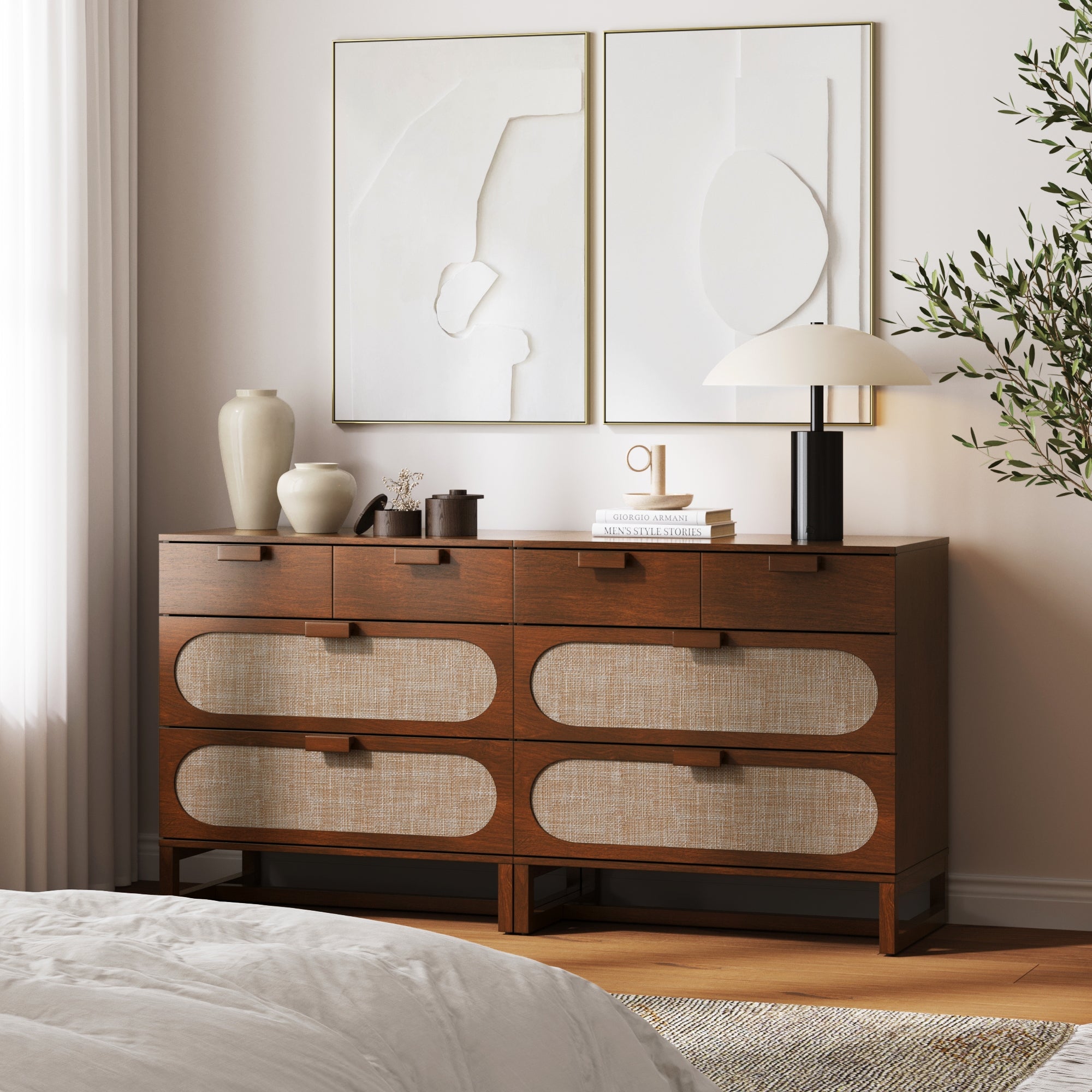 A pair of Nathan James Mid-Century Rattan 3-Drawer Dressers in Dark Acacia hold vases, books, and a lamp. Two abstract artworks hang above, while a leafy plant stands to the right. Sunlight filters through white curtain panels nearby.