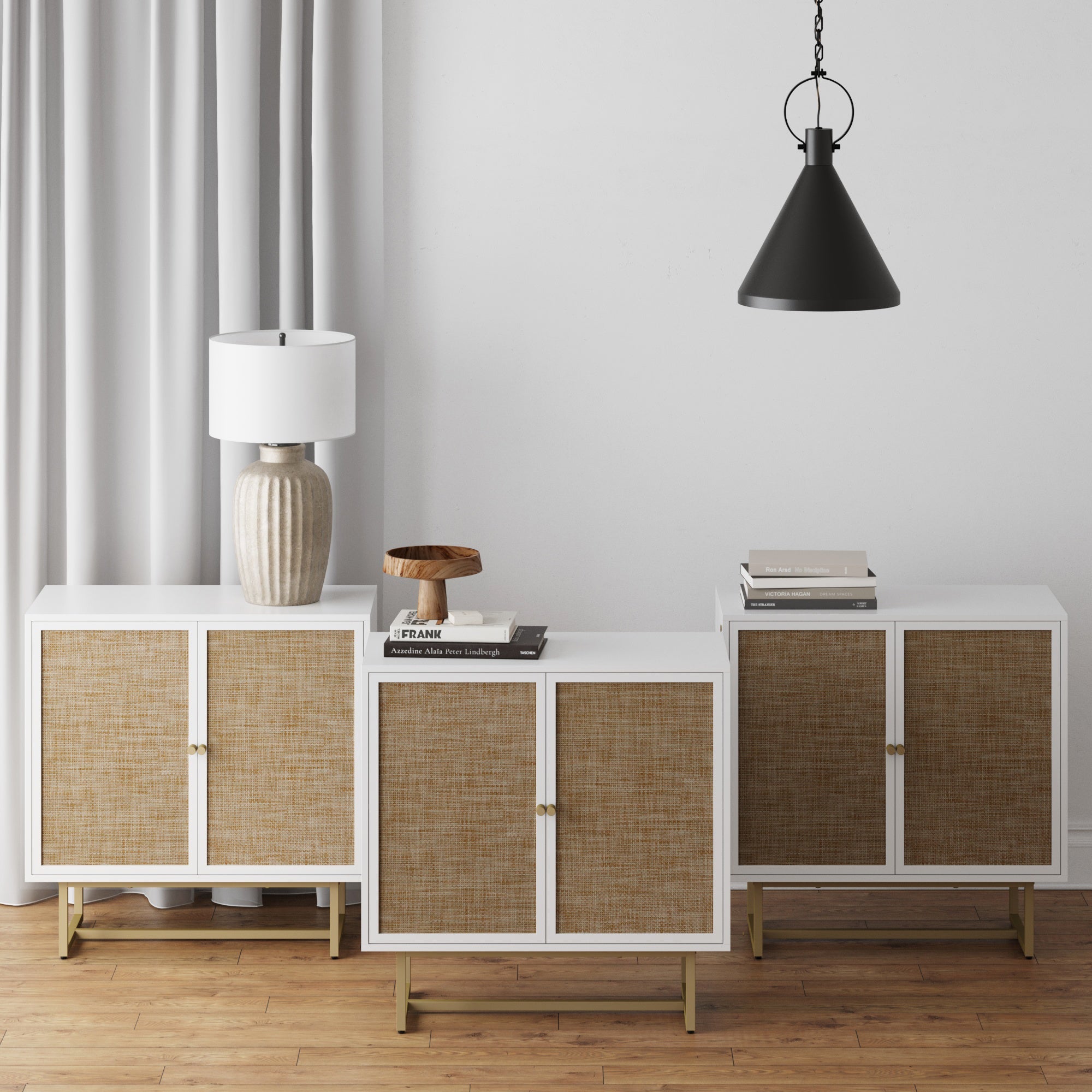 The Nathan James Rattan TV Console Credenza White (Set of 3) stands on a wooden floor, topped with a beige lamp, books, and tray. A black pendant light hangs above before a white wall and gray curtain.