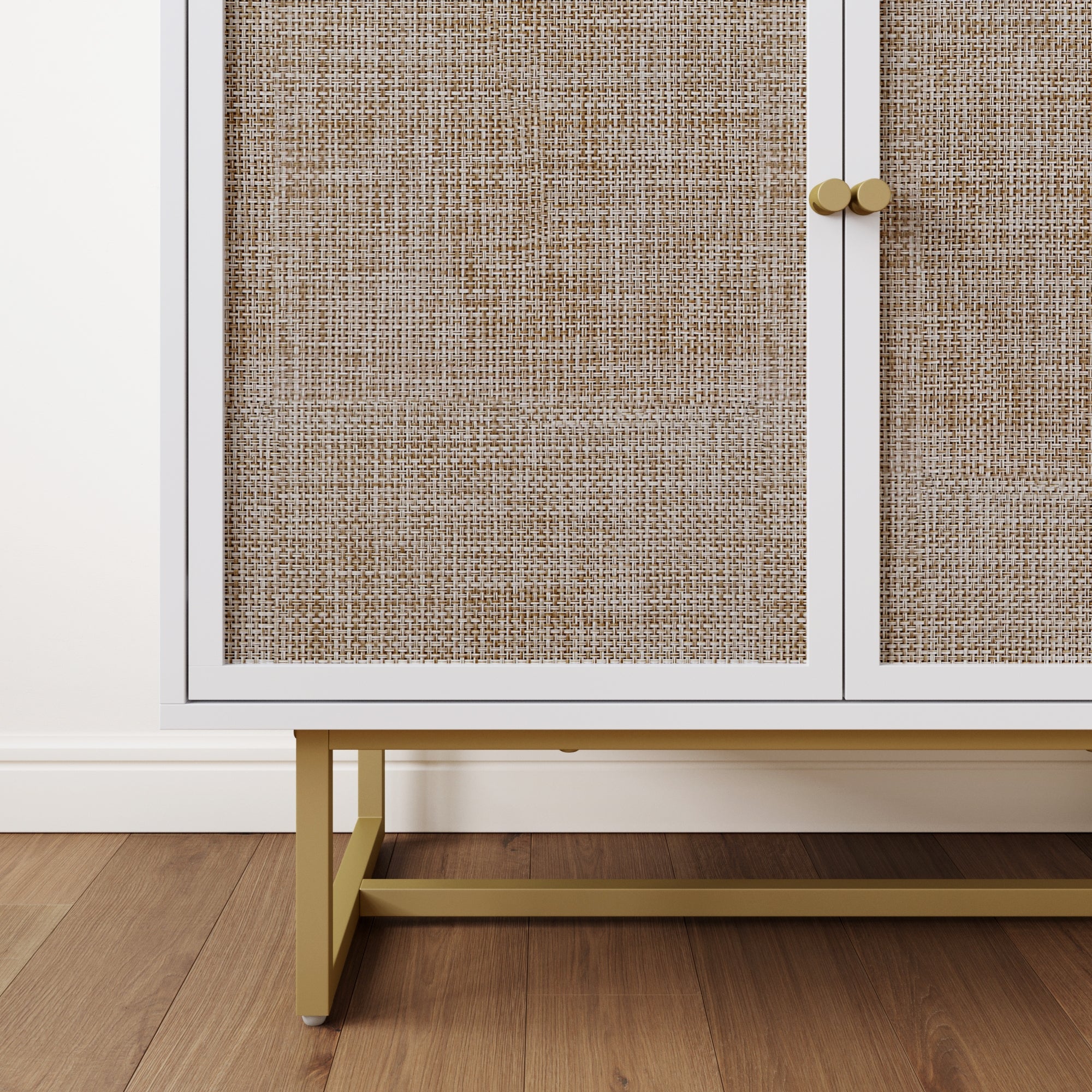 A close-up of a cabinet with woven rattan doors, white frame, gold handles, and gold metal legs. The cabinet sits on a wooden floor against a white wall with a white baseboard.