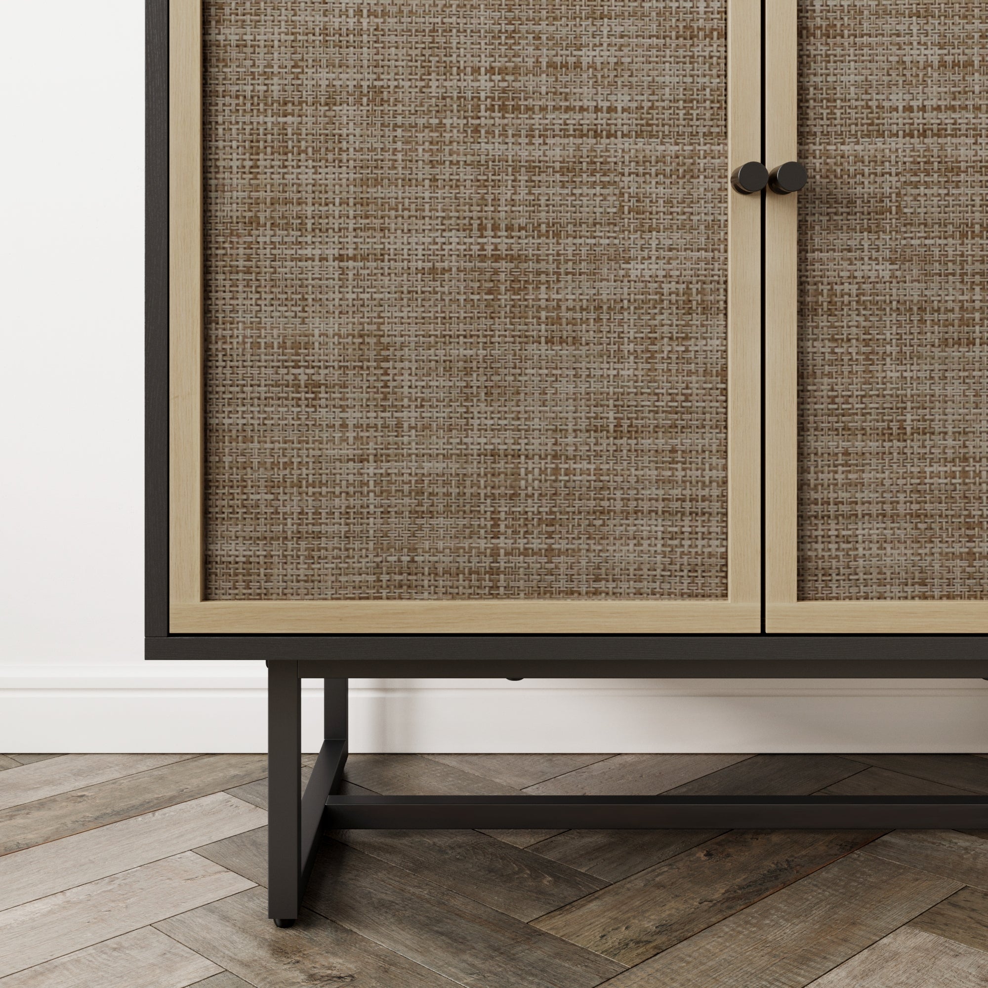 Close-up of the lower section of a cabinet with textured woven doors, black metal frame and legs, standing on a herringbone-patterned wood floor against a white wall.