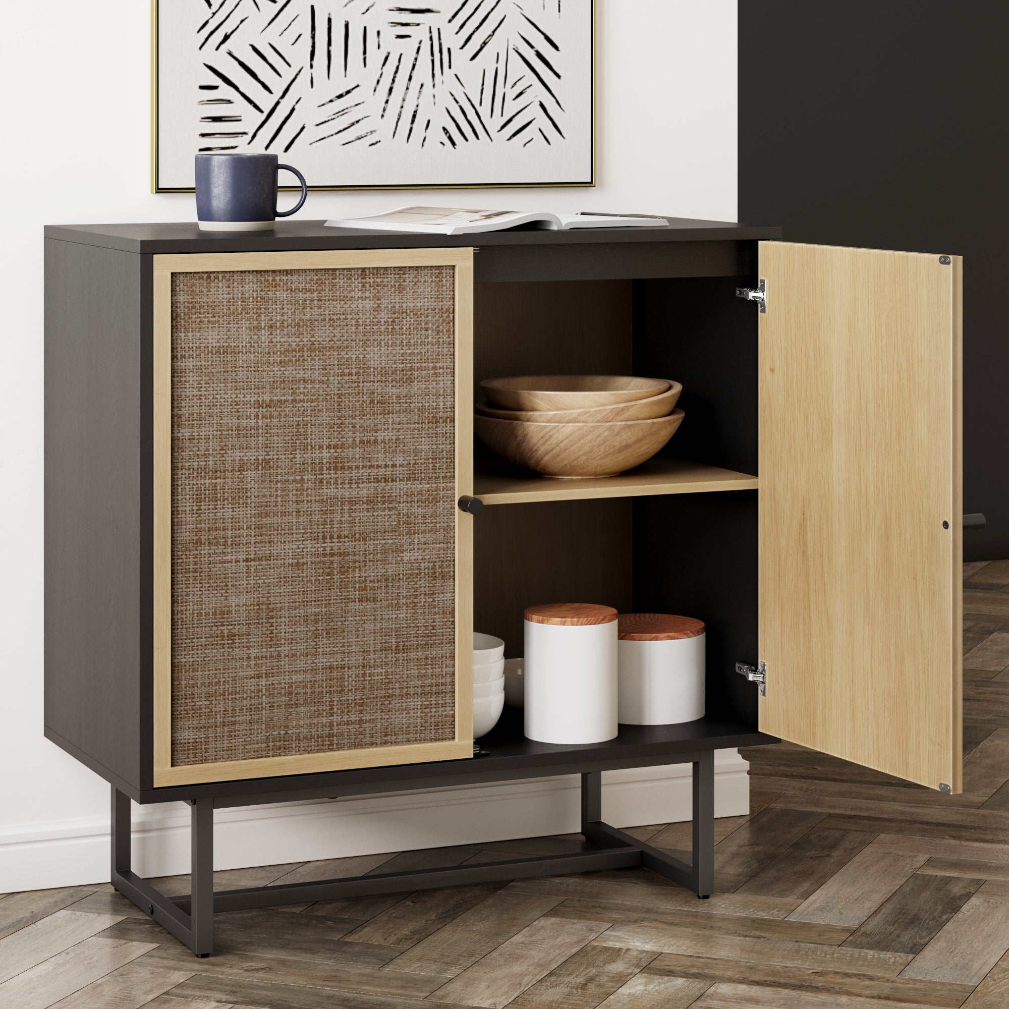 A modern cabinet with one door open reveals wooden bowls and white canisters inside. On top, theres a mug and an open book. The cabinet has a woven panel and stands on metal legs, placed on a herringbone wood floor.