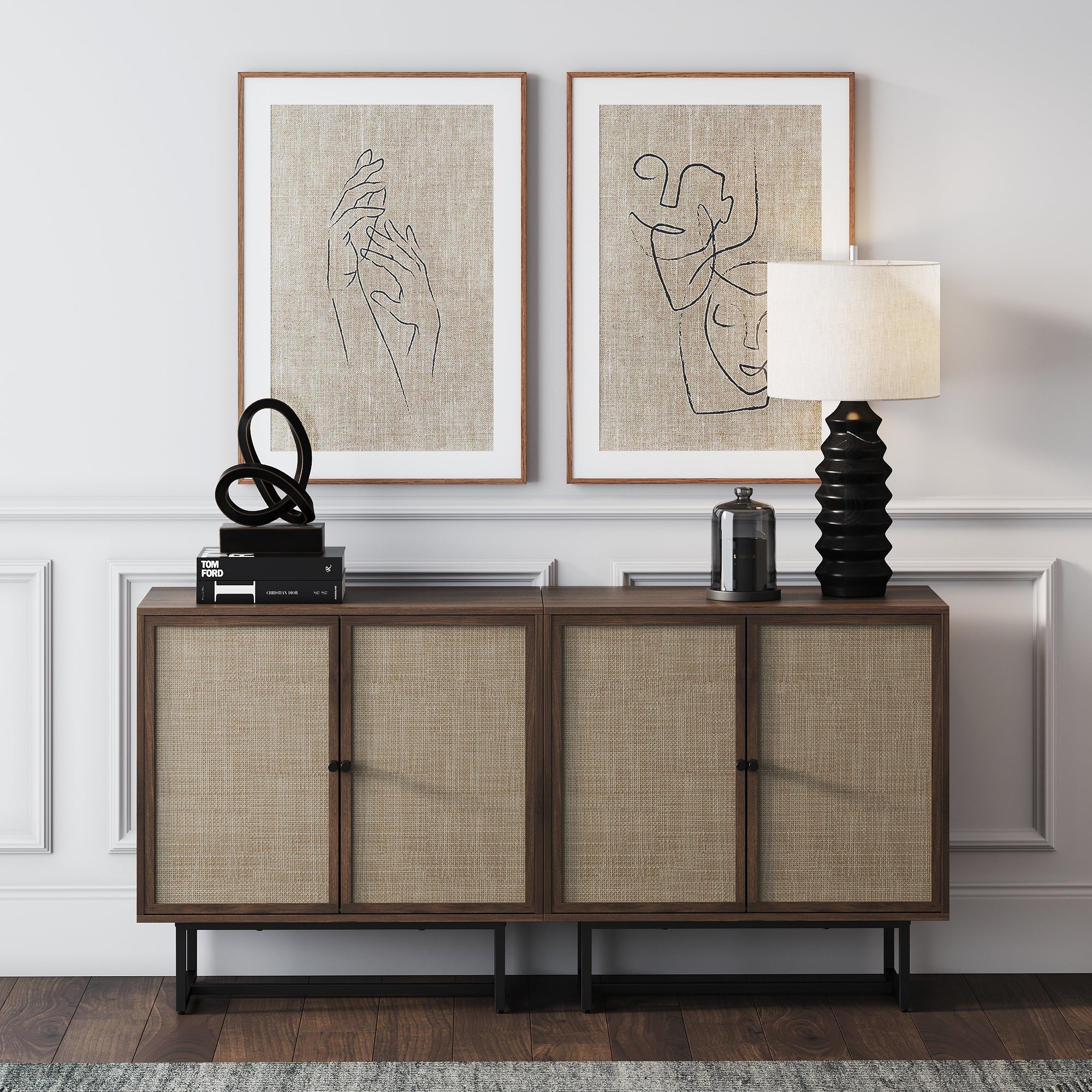 A modern sideboard with woven cabinet doors sits against a white paneled wall, topped with a sculptural black decor piece, a table lamp, and a jar. Two minimalist line art prints are hung above the sideboard.