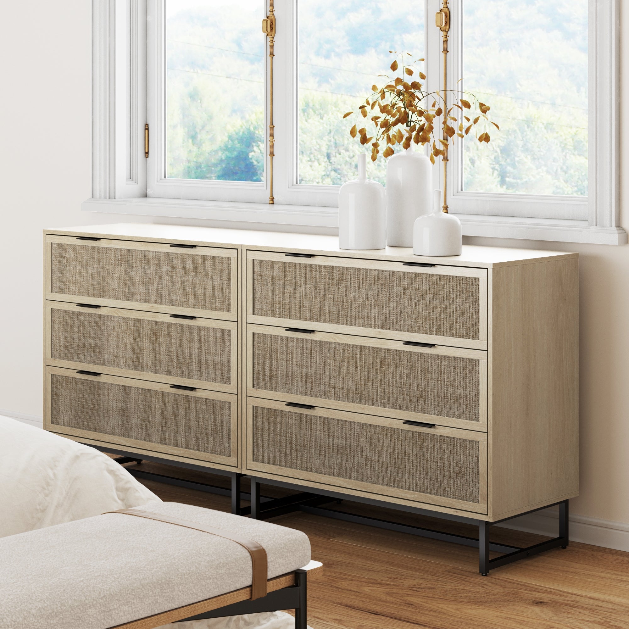 A light wood dresser with eight woven rattan drawers stands by a window. Three white vases holding dried branches sit on top, and natural light fills the minimal, modern bedroom.
