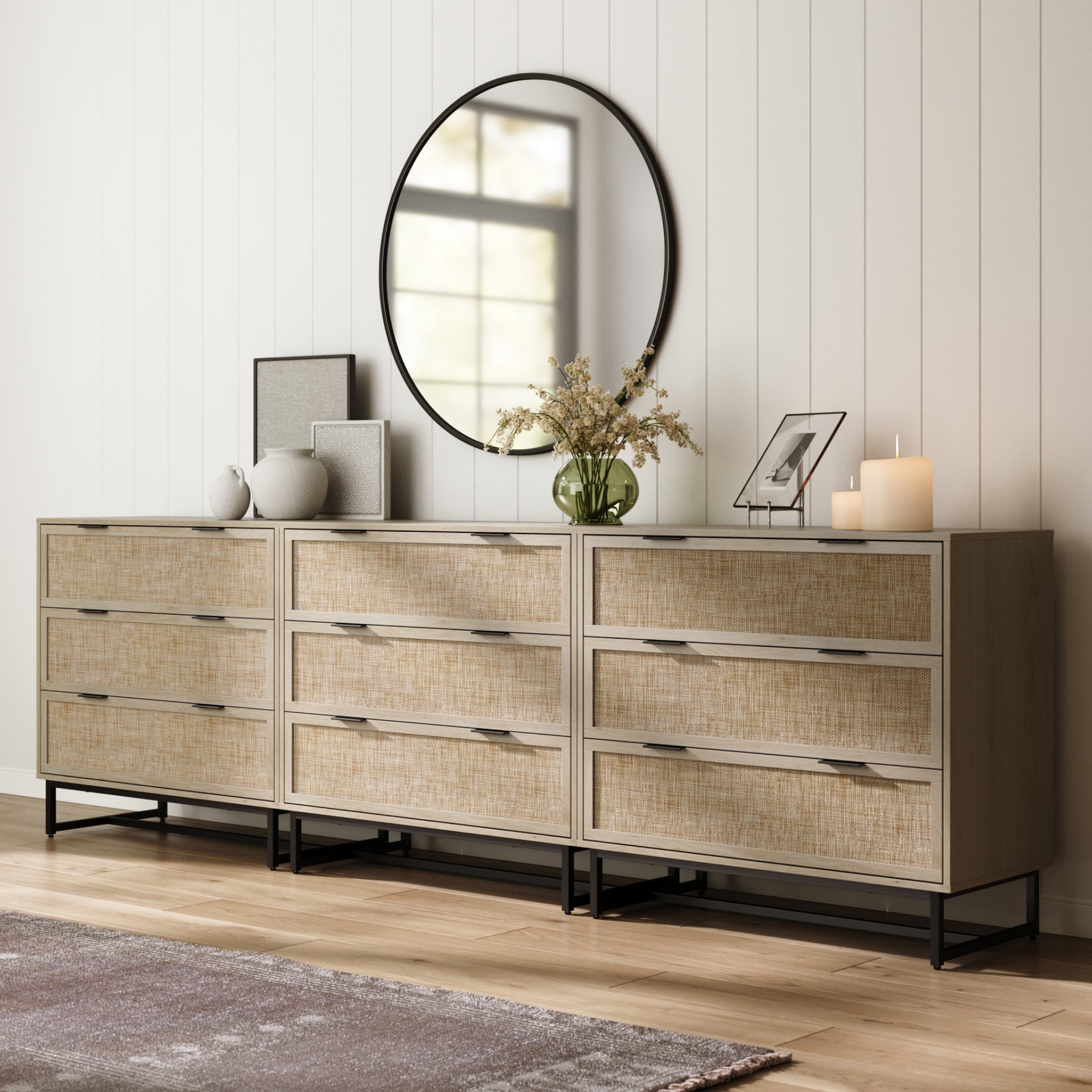 Modern bedroom with Nathan James Rattan, Wood & Metal 3-Drawer Large Dresser Oak (Set of 3), topped with vases, dried flowers, art, and candles against a white paneled wall and wooden floor.