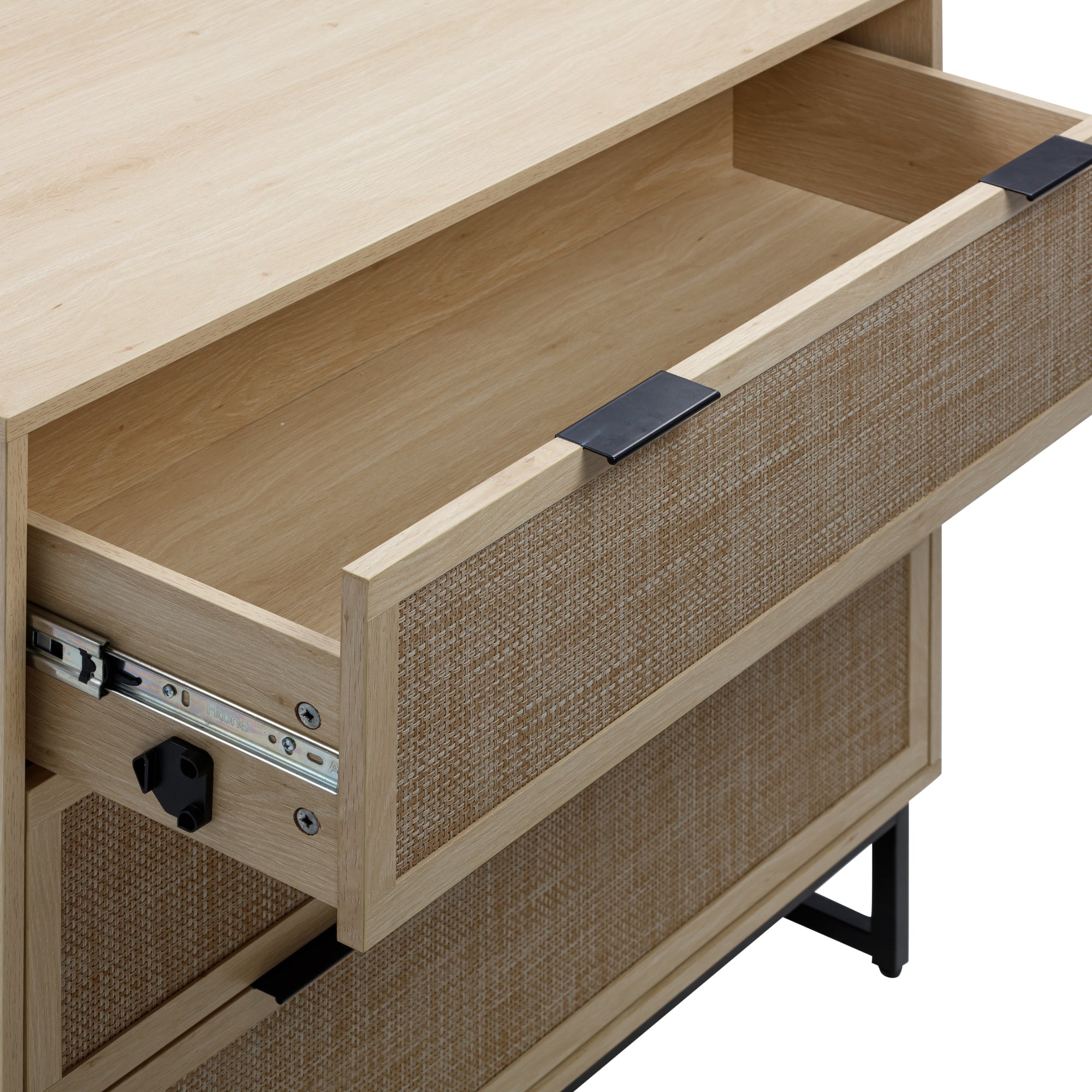 A close-up of a light wood dresser with a woven rattan front; one drawer is open, showing the empty wooden interior and black metal handles, with black metal legs visible at the bottom.