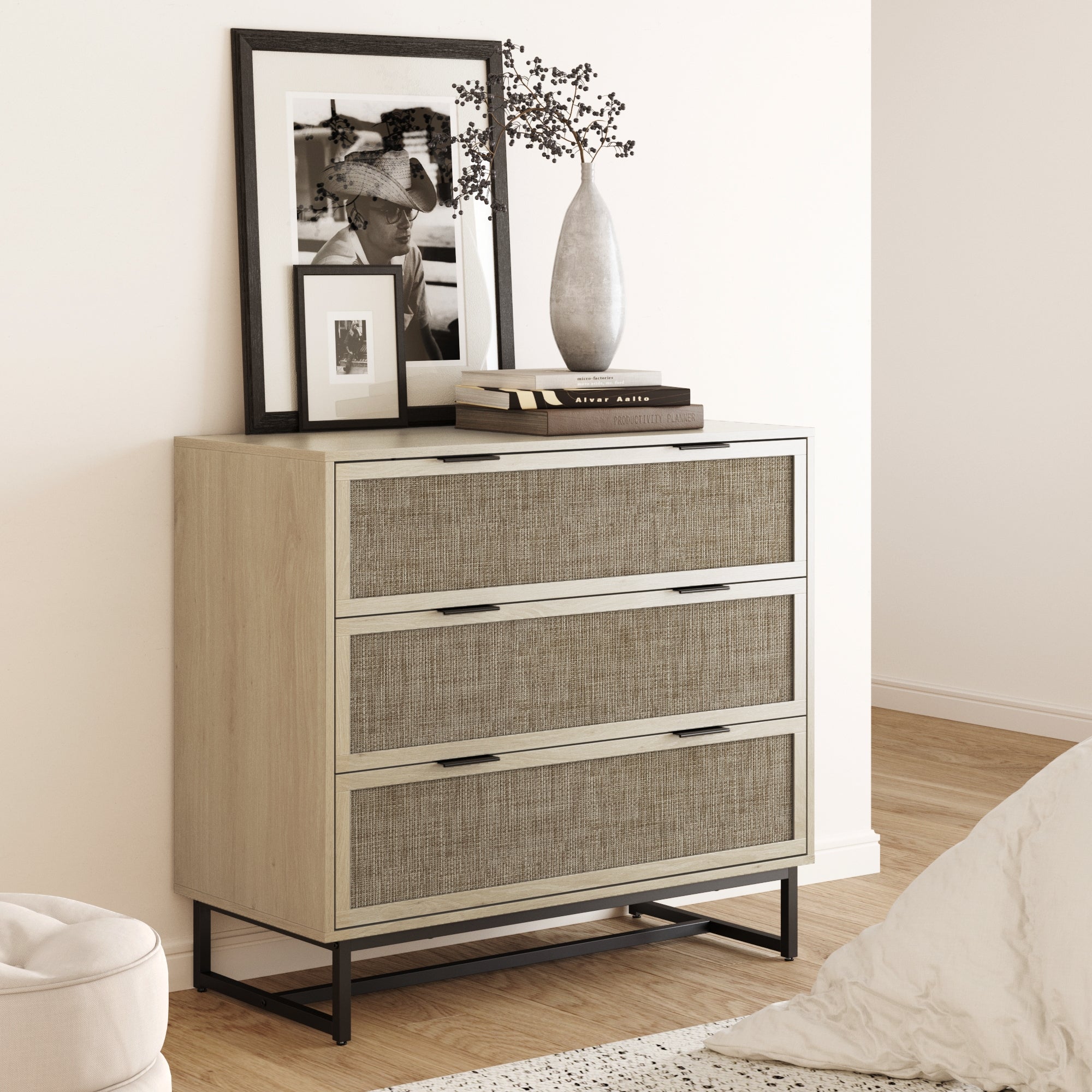 The Nathan James Rattan, Wood & Metal 3-Drawer Dresser in Oak features textured drawers and black metal legs. Style it with framed photos, books, and a vase for a cozy, modern bohemian look in any minimal space.