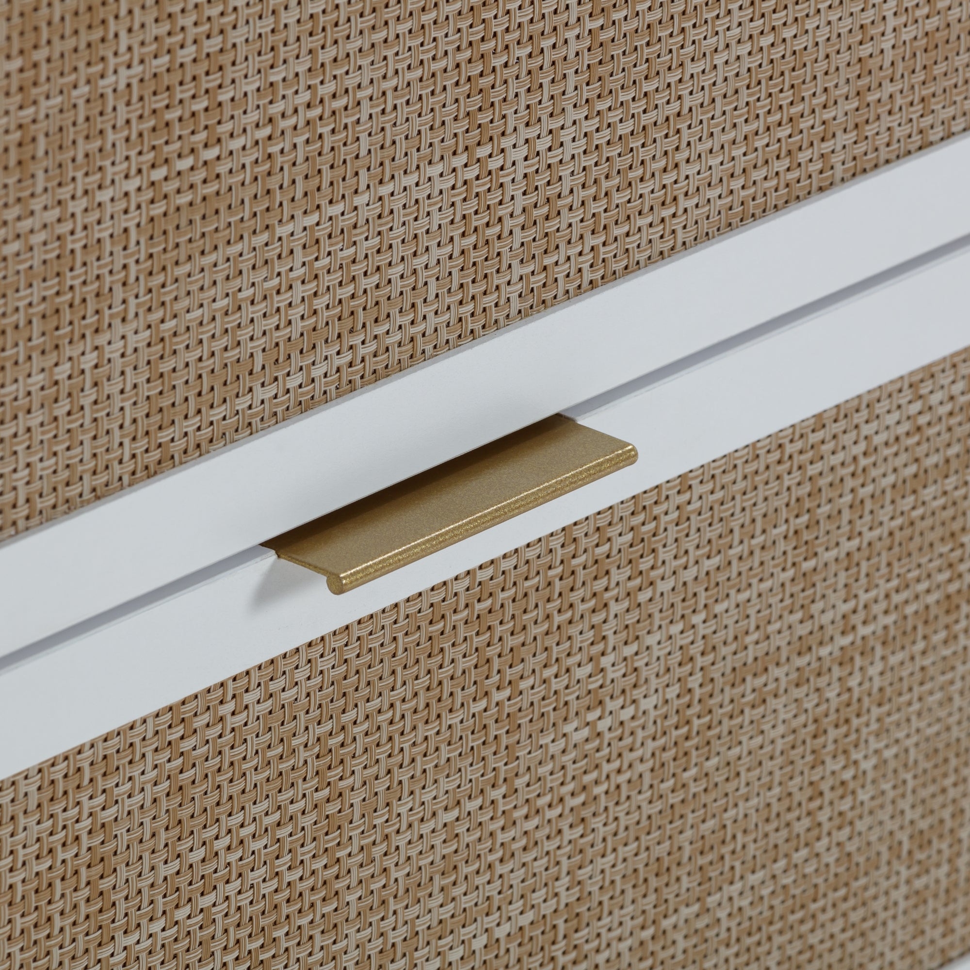 Close-up of a drawer with a woven rattan front, featuring a simple gold handle and a white horizontal trim.