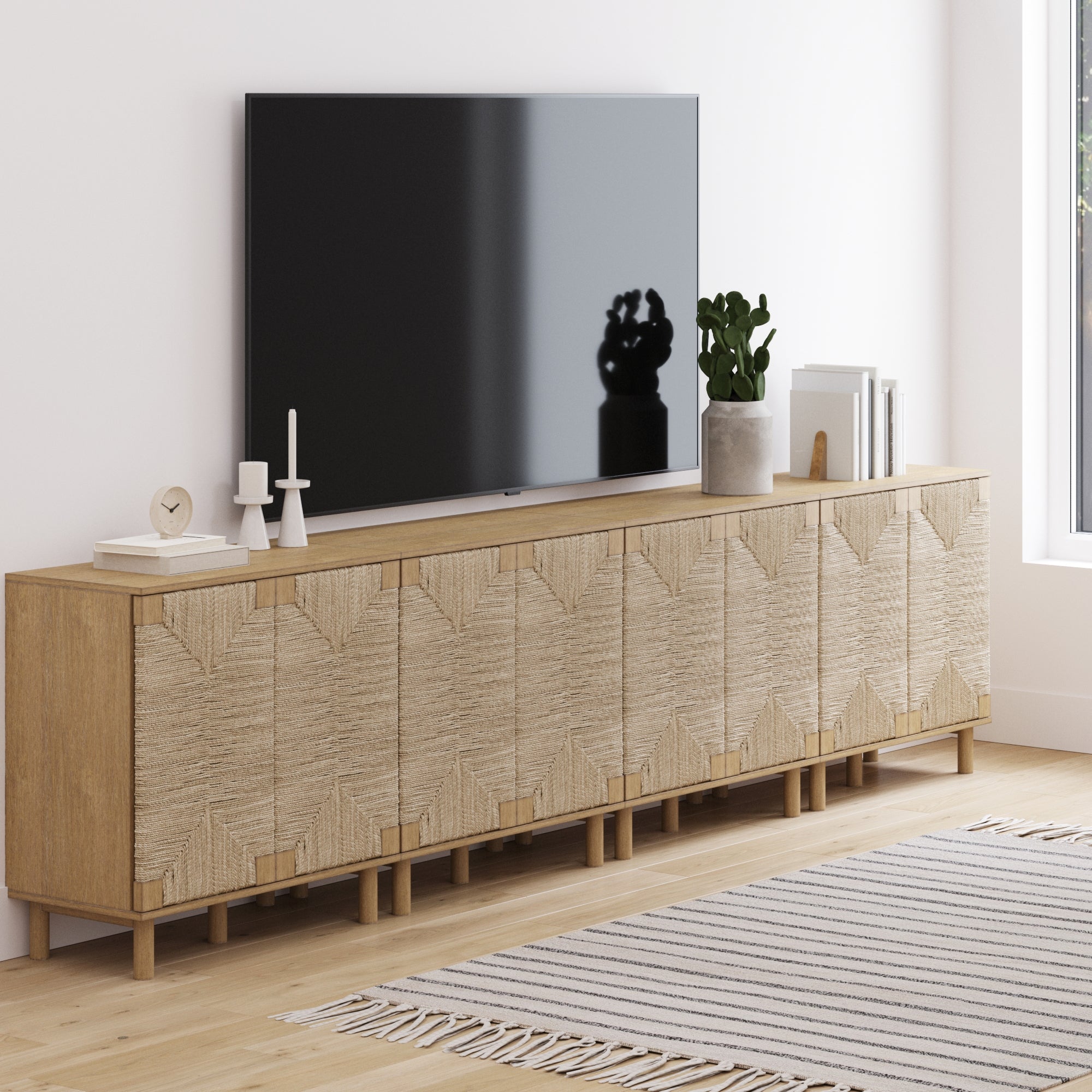 A TV rests on the Nathan James Large Seagrass TV Console Credenza (Set of 4), featuring stylish seagrass cabinet doors that bring natural elegance to your space.