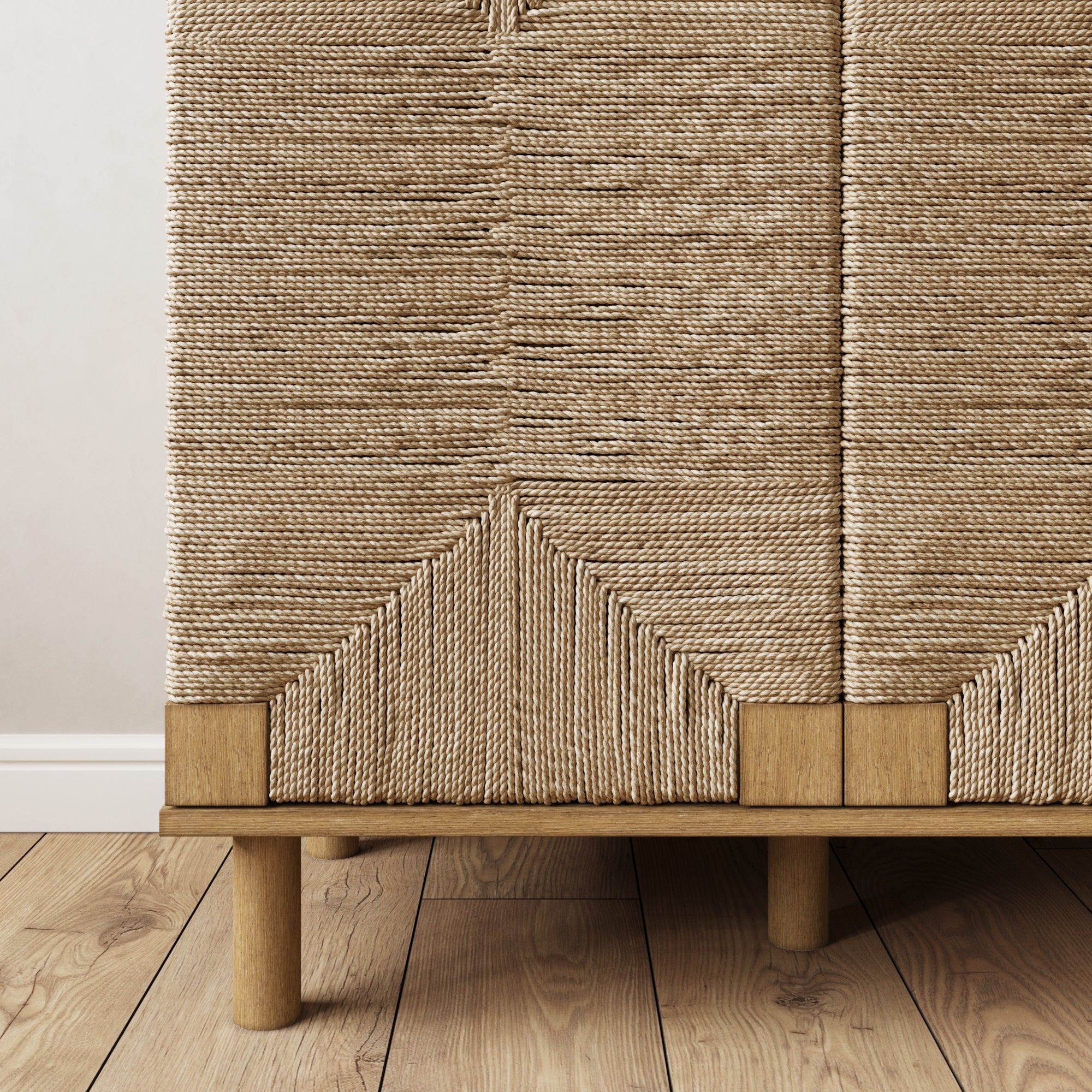 Close-up of a woven cabinet with intricate, geometric rope patterns on the doors. The cabinet has a natural wood frame and round wooden legs, placed on a light wooden floor against a plain light wall.