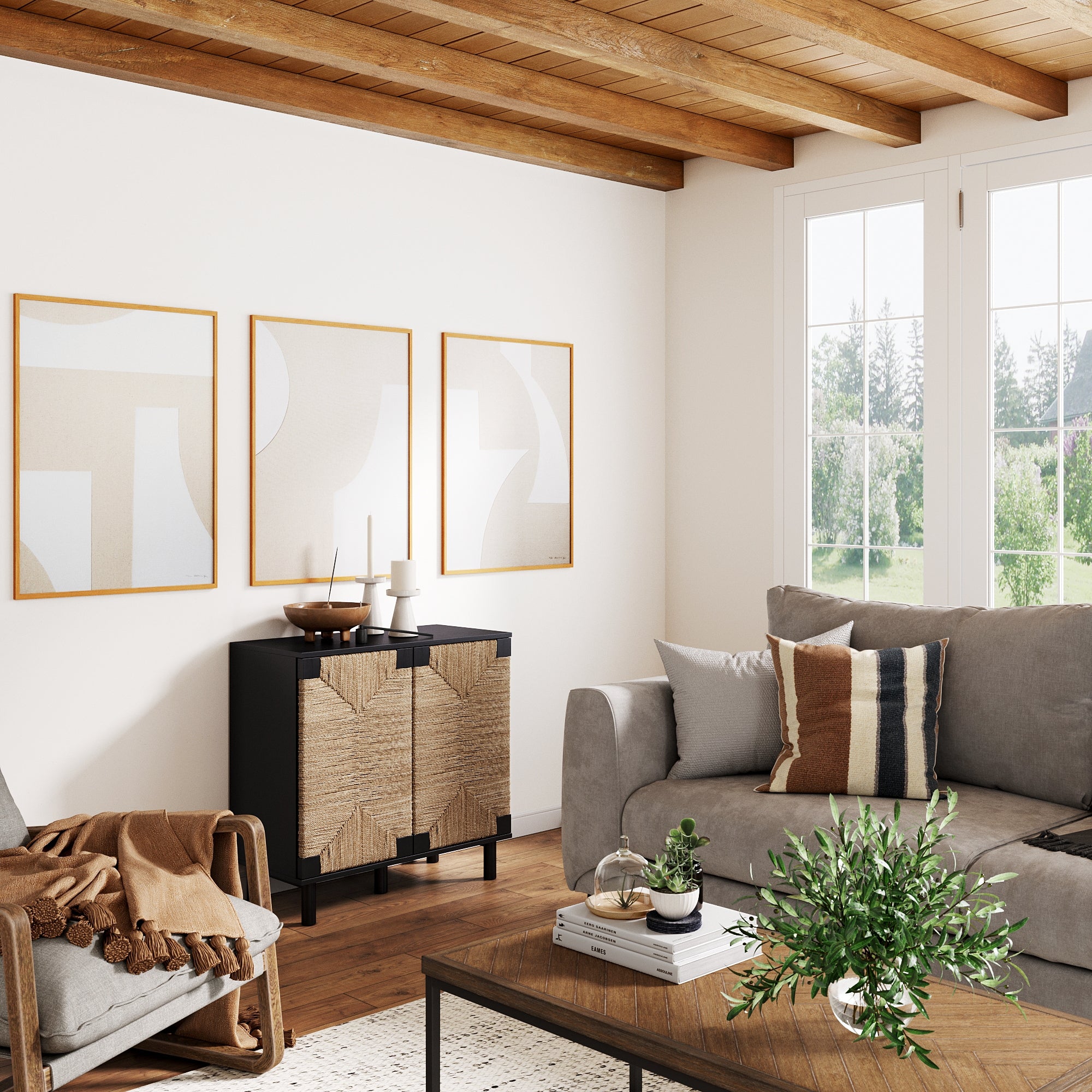 A modern living room with a gray sofa, neutral-toned pillows and blanket, a black cabinet with textured doors, abstract art on the wall, a coffee table with plants, and large windows letting in natural light.