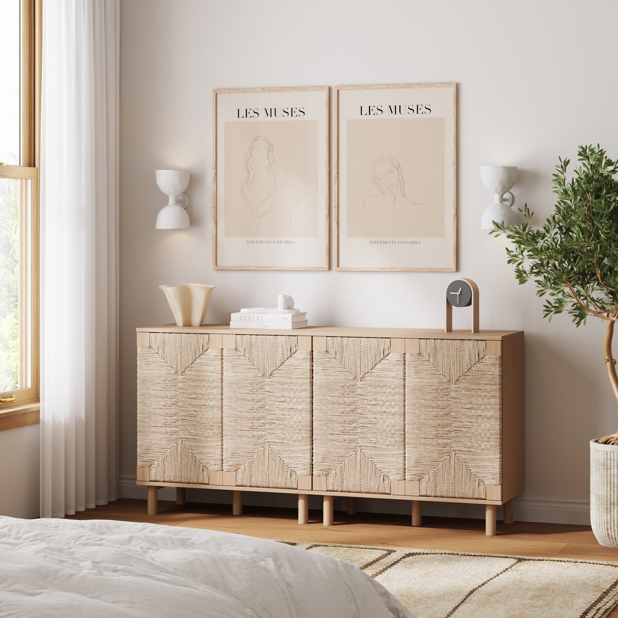 A minimalist bedroom features a Nathan James Seagrass TV Console Credenza in raw oak (set of 2) with natural seagrass doors, two abstract art prints above, modern wall sconces, decorative accents, a potted plant, and airy white curtains.
