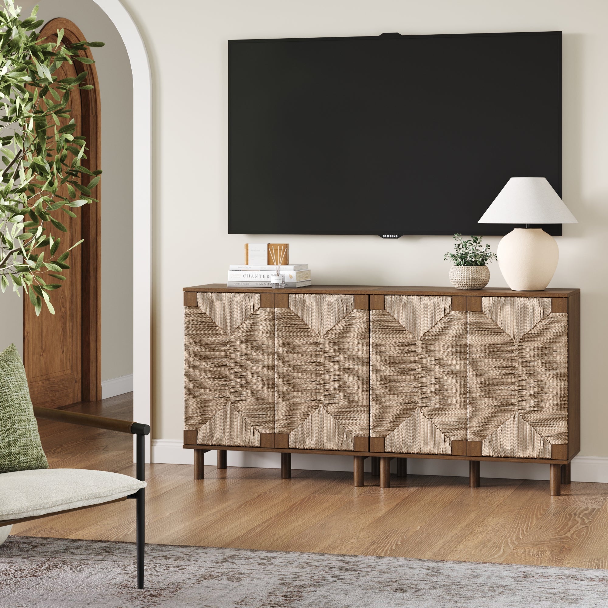 A modern living room features a large wall-mounted TV above the Nathan James Seagrass TV Console Credenza Dark Brown (Set of 2), styled with books, a lamp, a vase with greenery, and a bowl; bohemian flair comes from woven details and a potted plant.