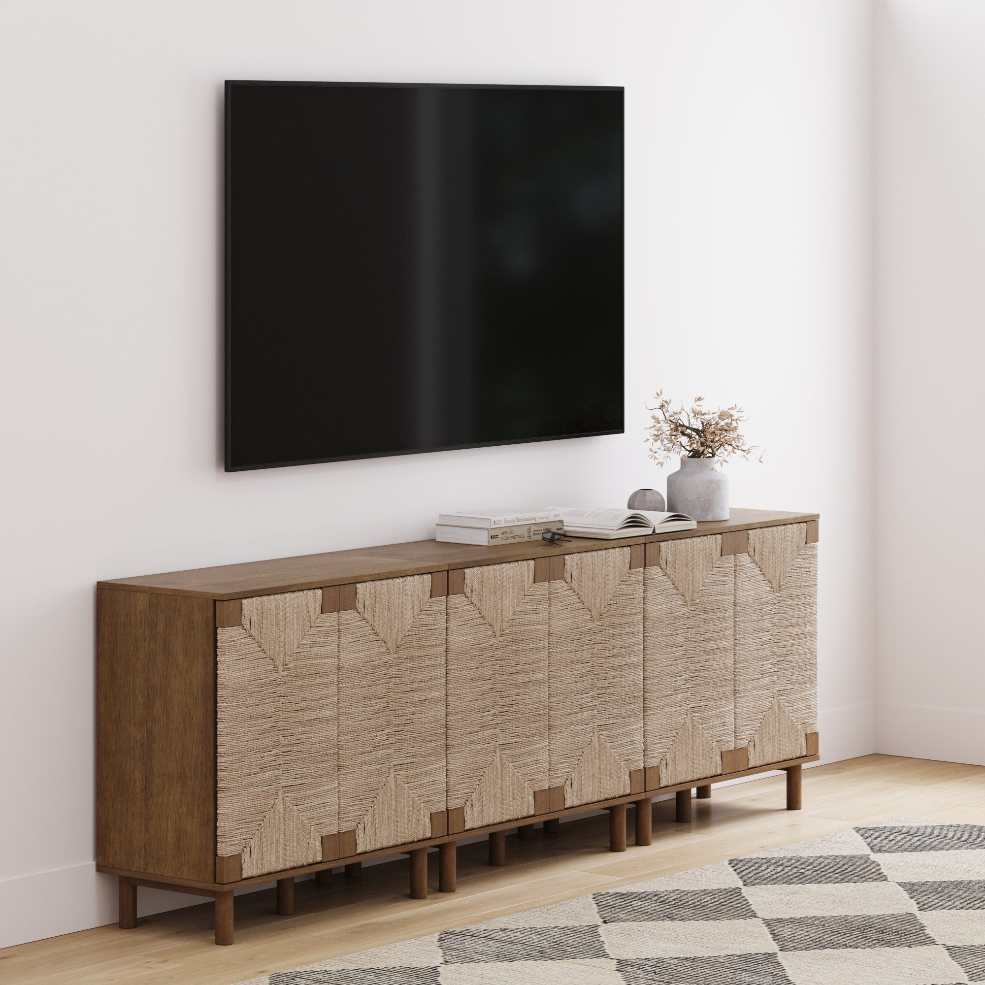 A modern living room features a wall-mounted TV above the Nathan James Seagrass TV Console Credenza Dark Brown (Set of 3), with textured storage, bohemian accents, and decor atop the sideboard, while a patterned rug adds warmth to the floor.