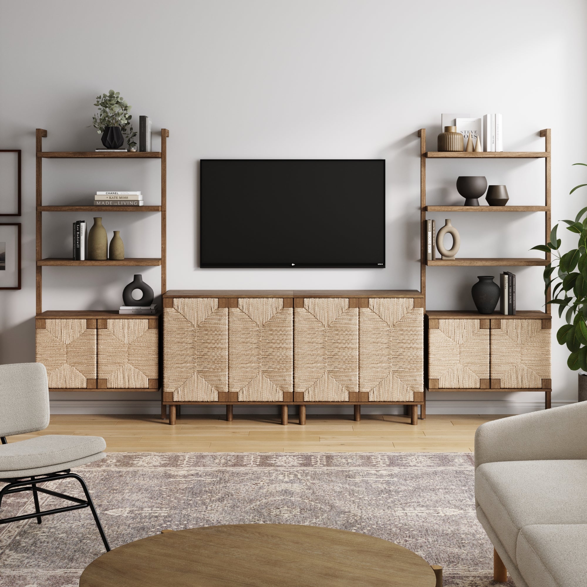 A modern living room features the Nathan James Seagrass TV Wall Unit Dark Brown (2 Cabinets) above a media console with seagrass doors, open shelves with decor, a rug, beige armchairs, a round wooden coffee table, and a potted plant.