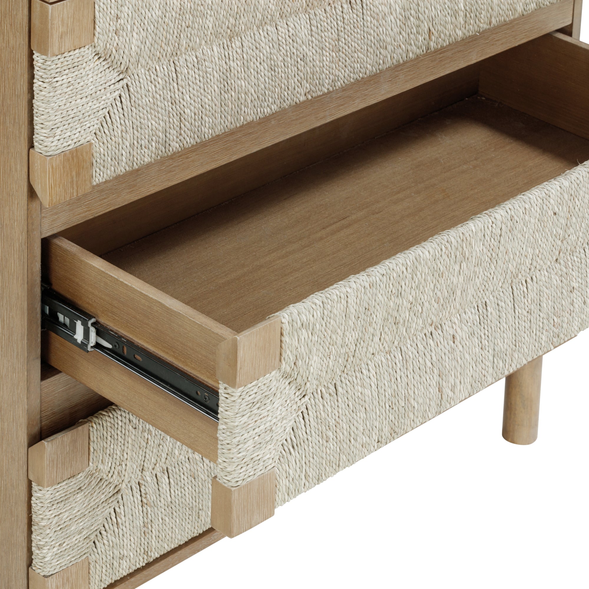 A close-up of a wooden drawer chest with a woven rope design, showing one drawer partially open on metal sliders. The chest has cylindrical wooden legs and natural, neutral-colored materials.