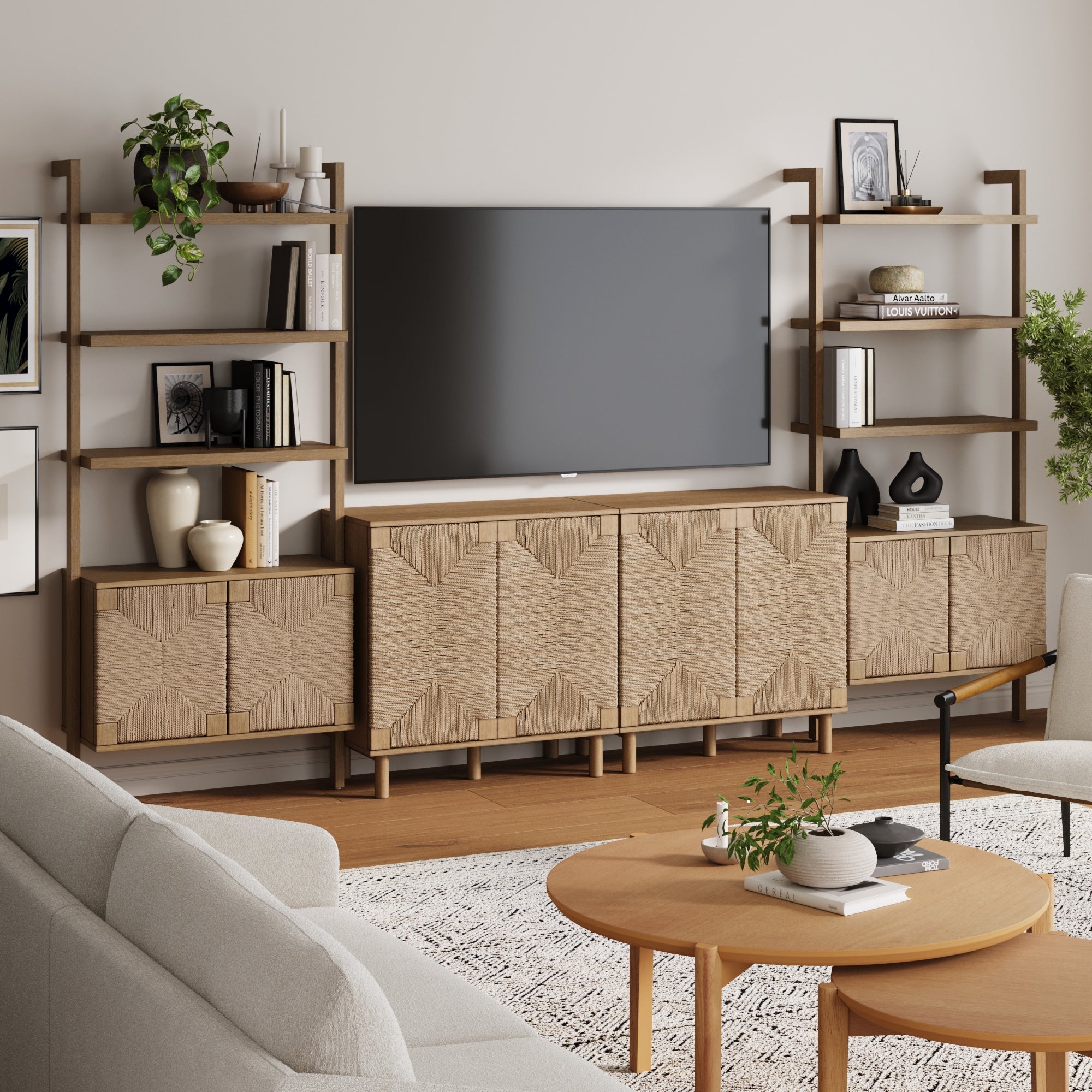 A modern living room showcases the Nathan James Seagrass Entertainment Center in brown, which supports a large TV on its sleek console. Open shelves display books and decor, complemented by a light sofa and round wooden coffee table.