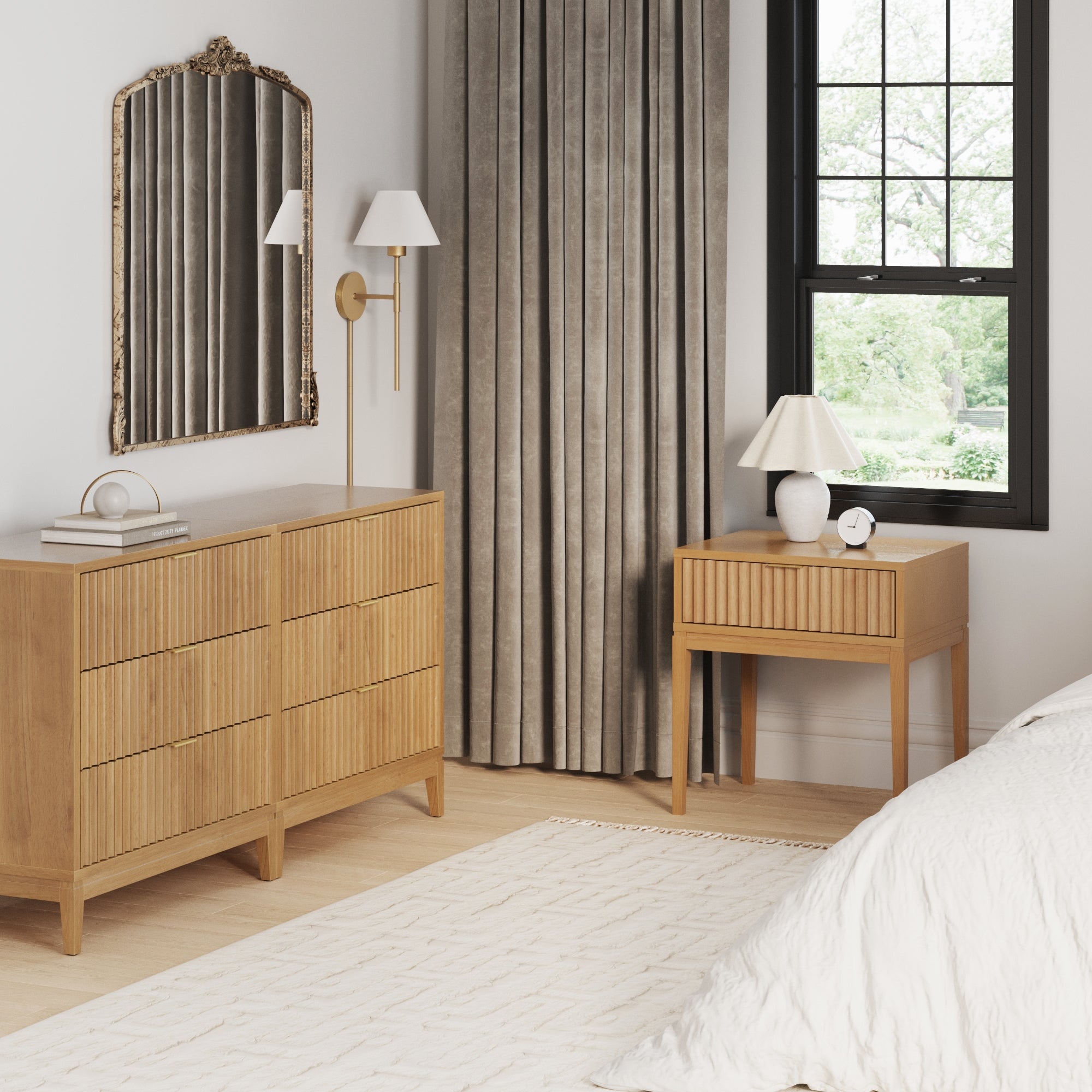 A modern bedroom featuring the Nathan James Fluted Wood Bedroom Set in Warm Pine, with fluted dresser drawers and a solid wood nightstand. A bed with a white comforter, decorative mirror, lamp, wall sconce, gray curtains, and natural light complete the look.