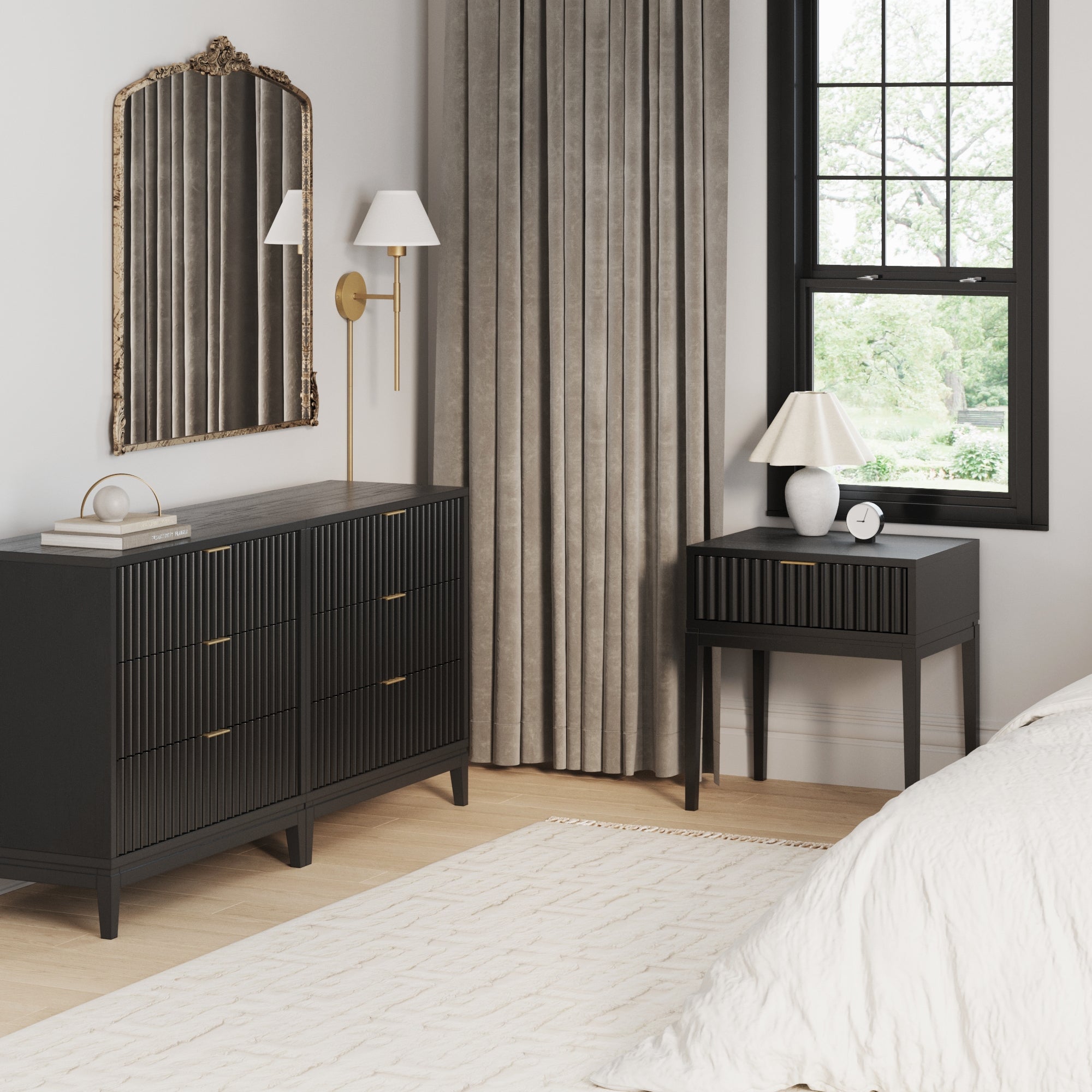 A modern bedroom corner featuring the Nathan James Fluted Wood Bedroom Set in Black Oak, paired with a solid wood nightstand, gold-framed mirror, wall sconce, beige curtains, table lamp, clock, and a bed with a white comforter on a light rug.