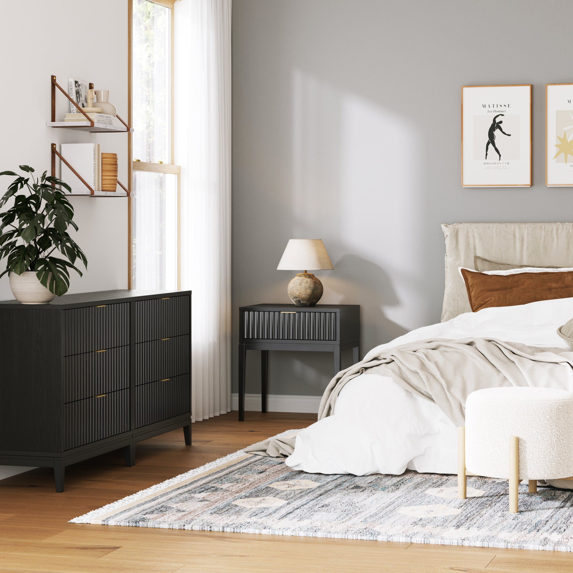 A modern, cozy bedroom with a gray accent wall, bed with neutral bedding, dark wood furniture, a potted plant, wall art, and a large window with sheer curtains letting in natural light.