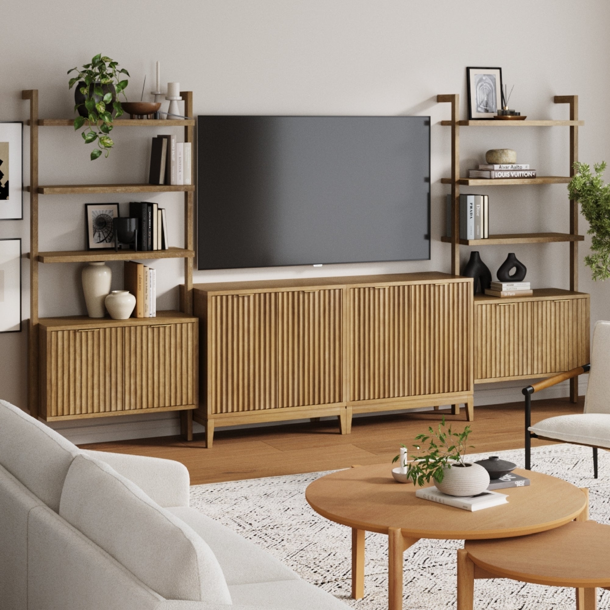 A modern living room showcasing the Nathan James Mid-Century Entertainment Center Light Brown (2 Cabinets), wall-mounted TV, wooden shelves, decorative vases, plants, books, framed art, a round coffee table, and a light-colored sofa and rug.