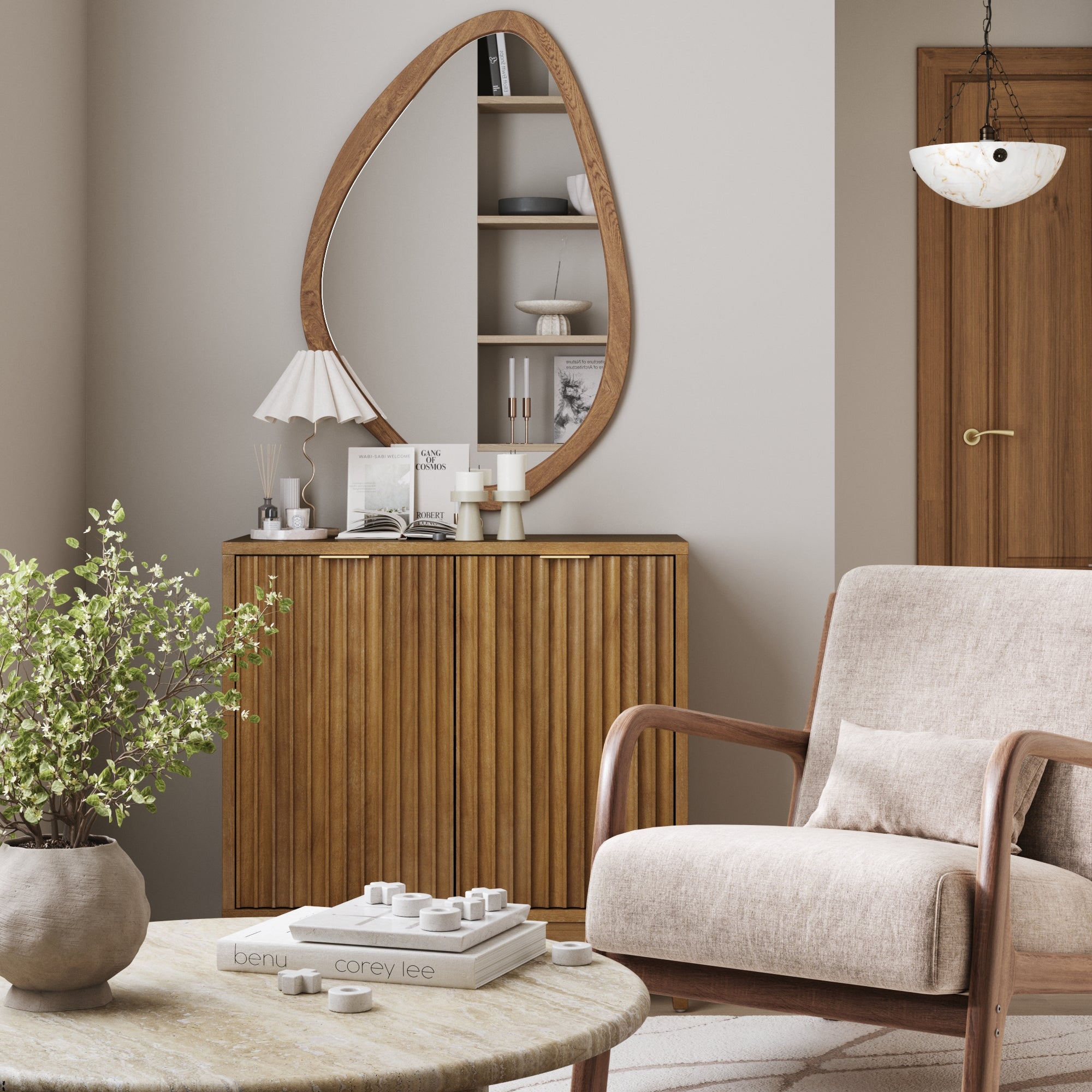 A cozy living room showcases a beige armchair, round table with plant and decor, a Nathan James Mid-Century Fluted Storage Cabinet in light brown, and an oval mirror above. Neutral tones and soft lighting complete the inviting look.