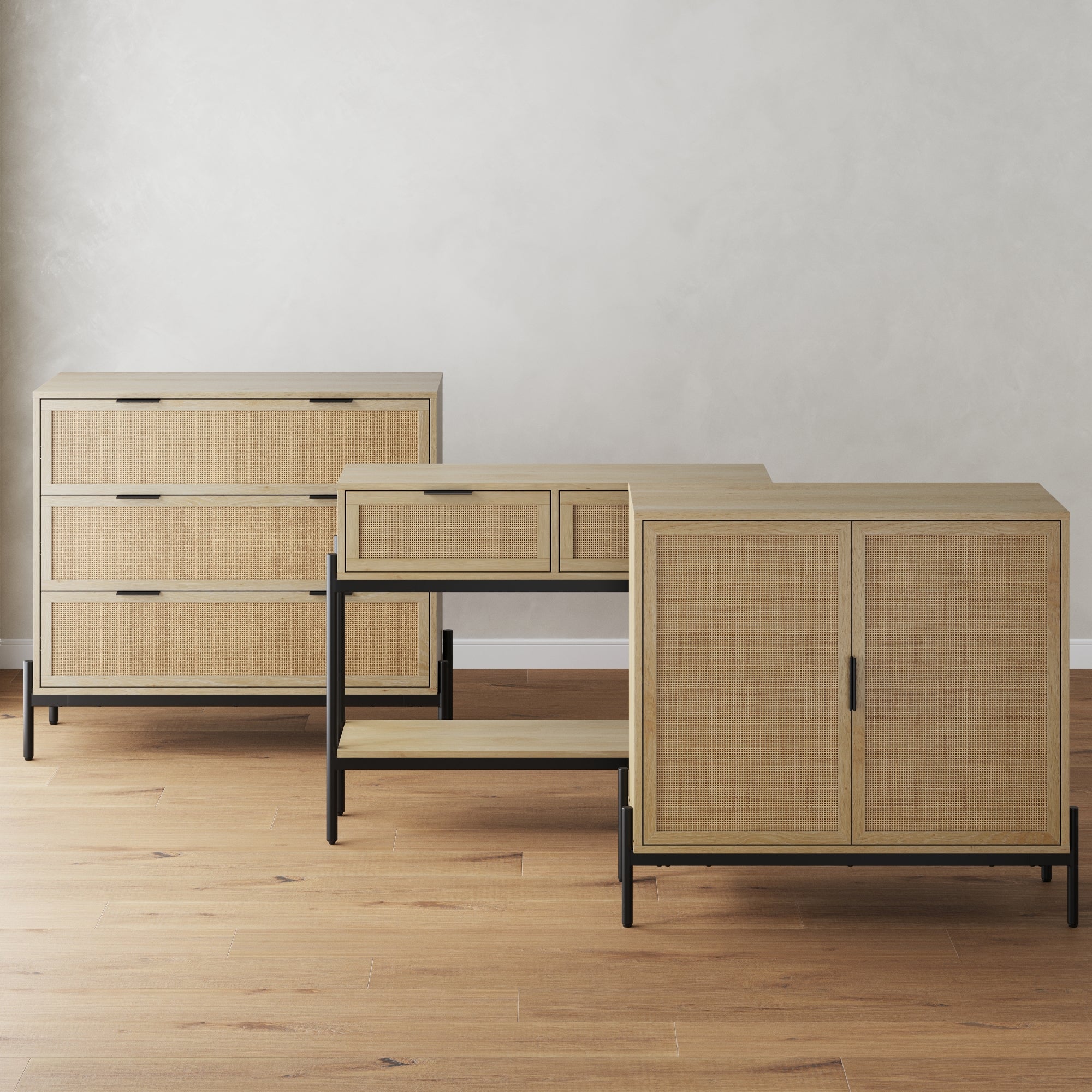 Three pieces of modern furniture with light wood and woven rattan fronts, black metal legs, and frames. They include a three-drawer dresser, a console table with shelves, and a two-door cabinet, all on a wooden floor.