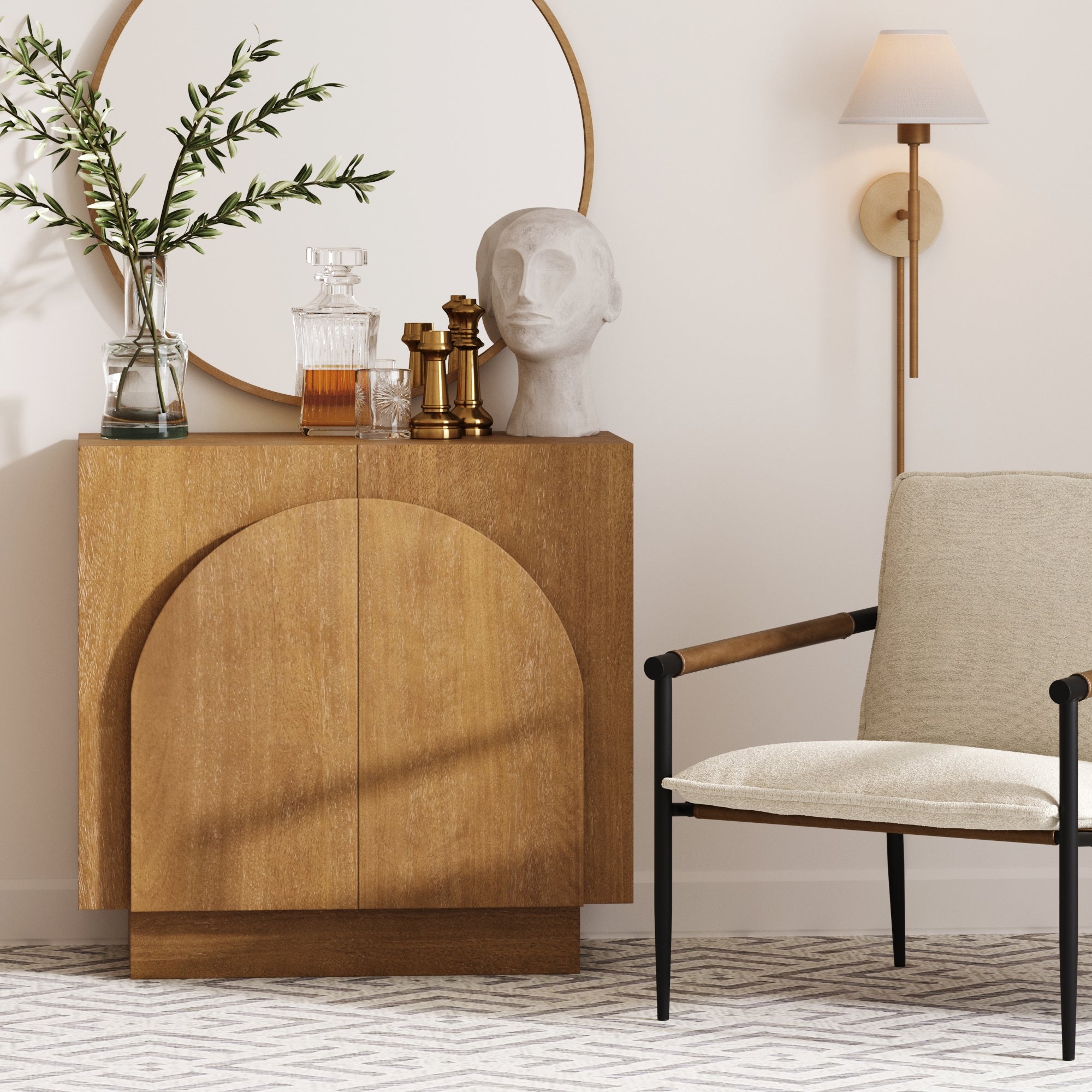 A modern living room corner with a wooden cabinet, a round mirror, glass decanters, a white sculpture, a brass wall sconce, and a beige armchair on a patterned rug.